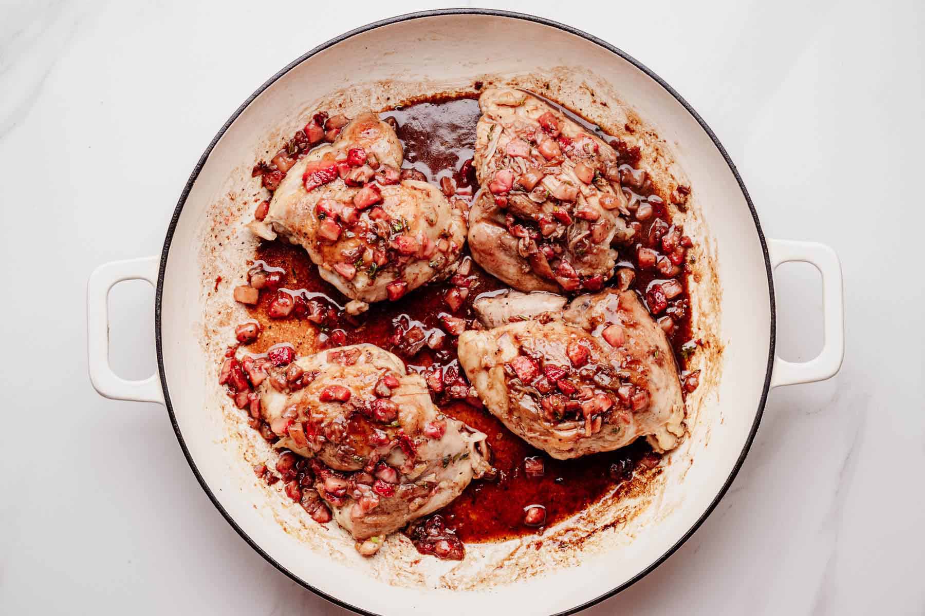 Cooked chicken thighs in a skillet coated with glossy strawberry balsamic glaze.