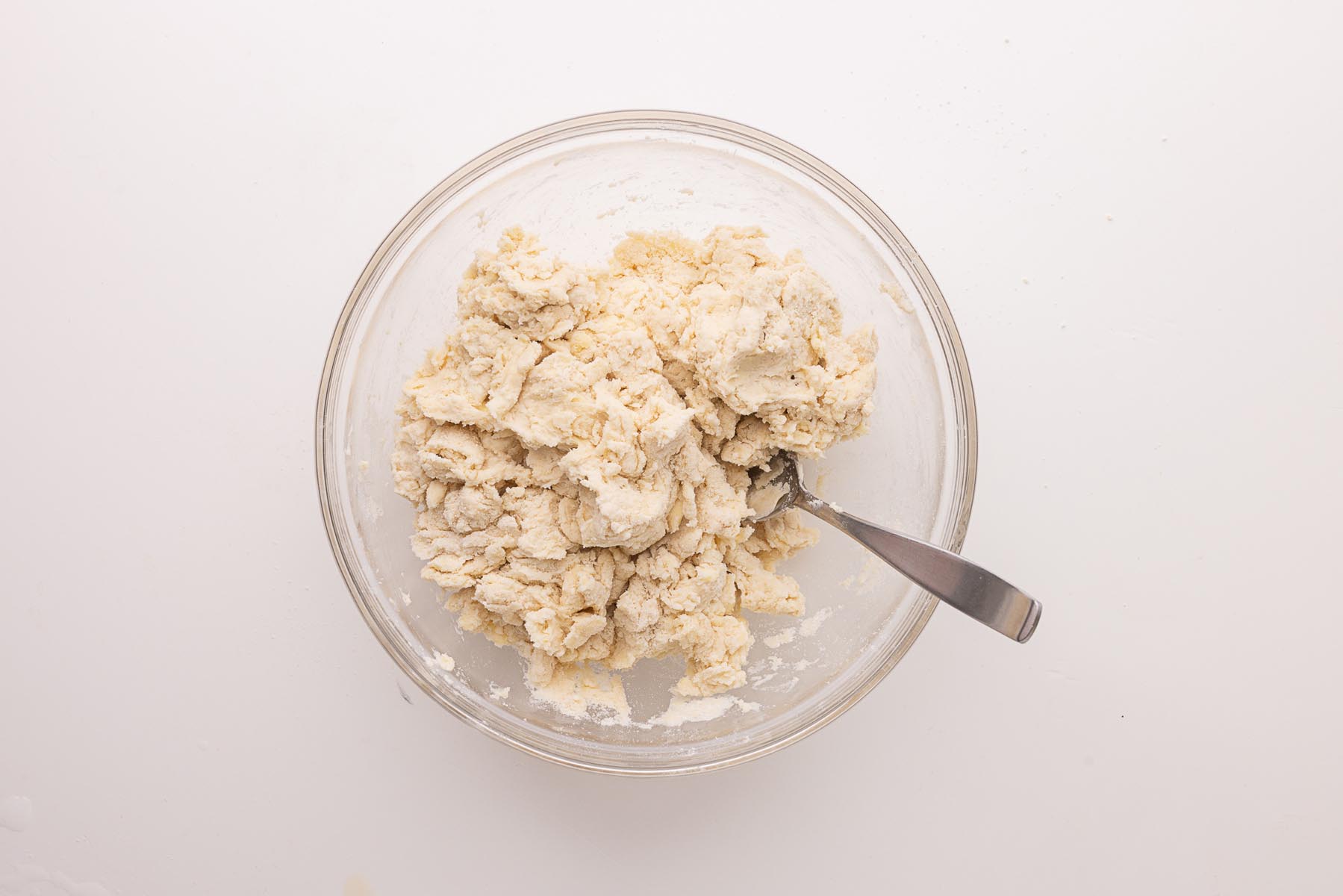 Shaggy pie dough in a glass bowl after adding water, with a fork used for gently combining the ingredients.