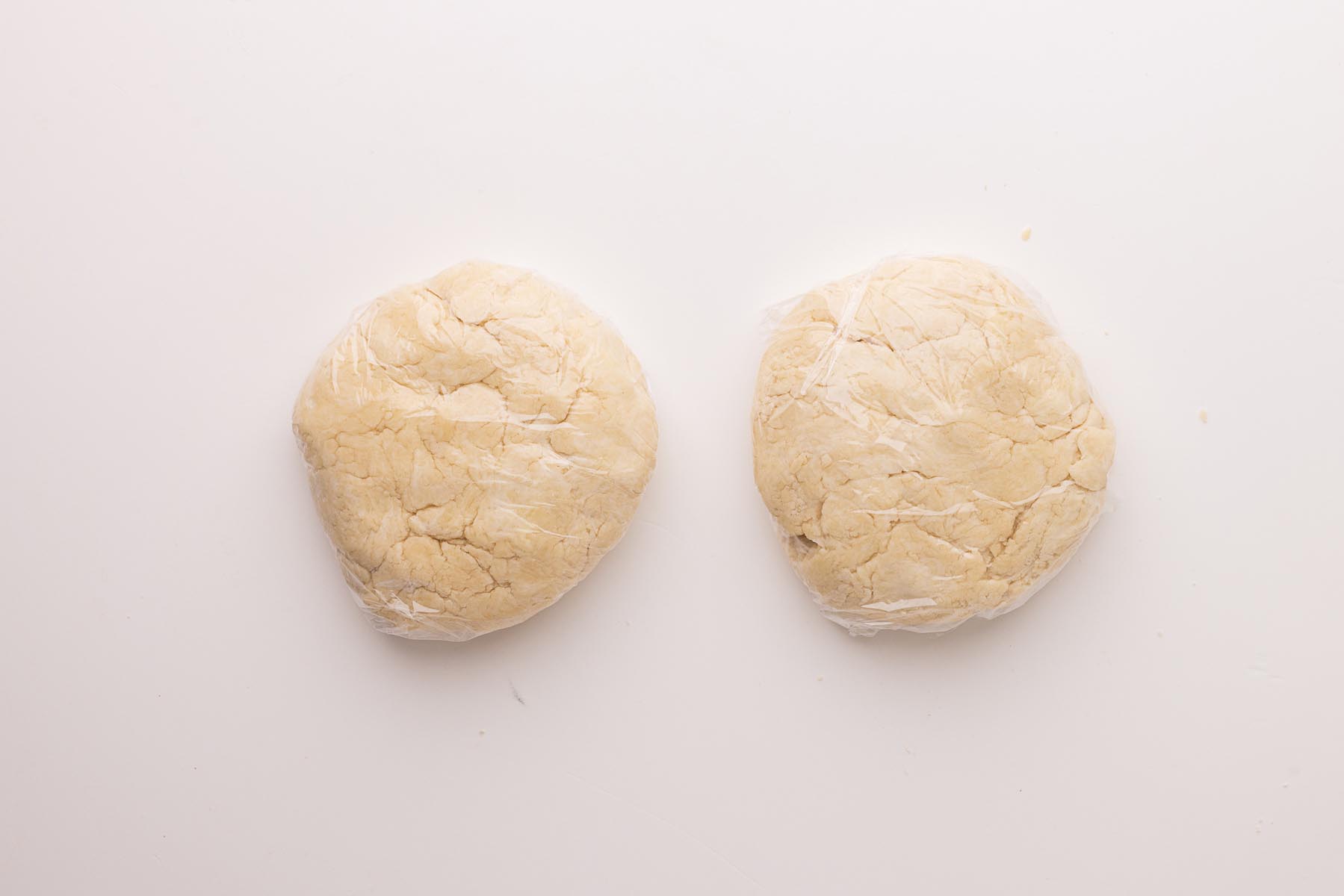 Two discs of pie dough wrapped in plastic wrap, ready to be chilled before rolling.