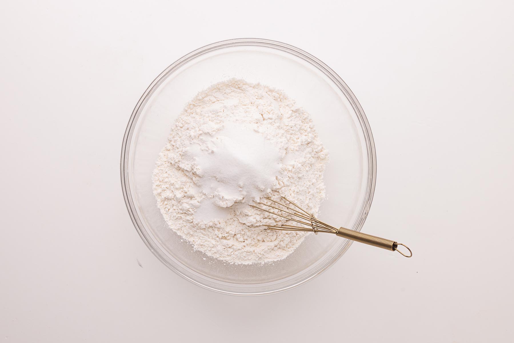 Flour, sugar, and salt combined in a glass mixing bowl with a gold whisk, ready to be mixed for homemade pie crust.