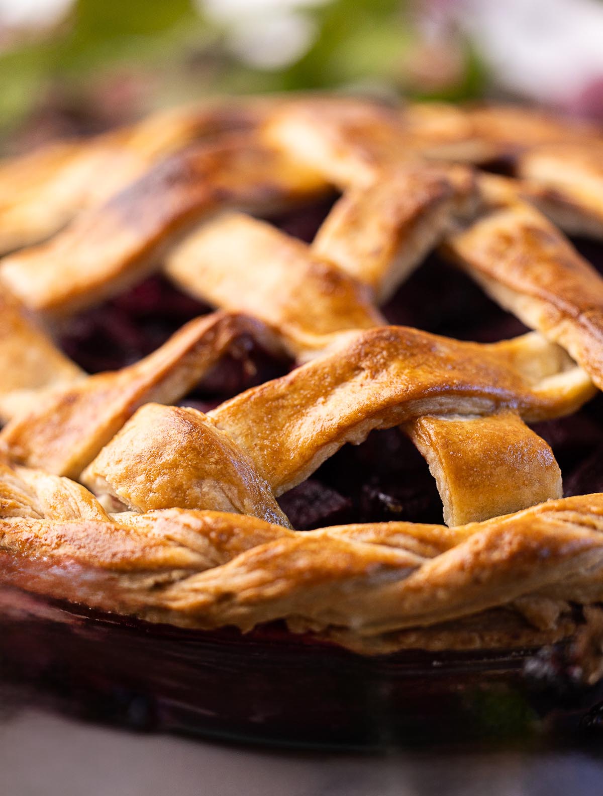 Golden brown lattice pie crust with a glossy finish, showing detailed texture of the flaky pastry over a dark fruit filling.