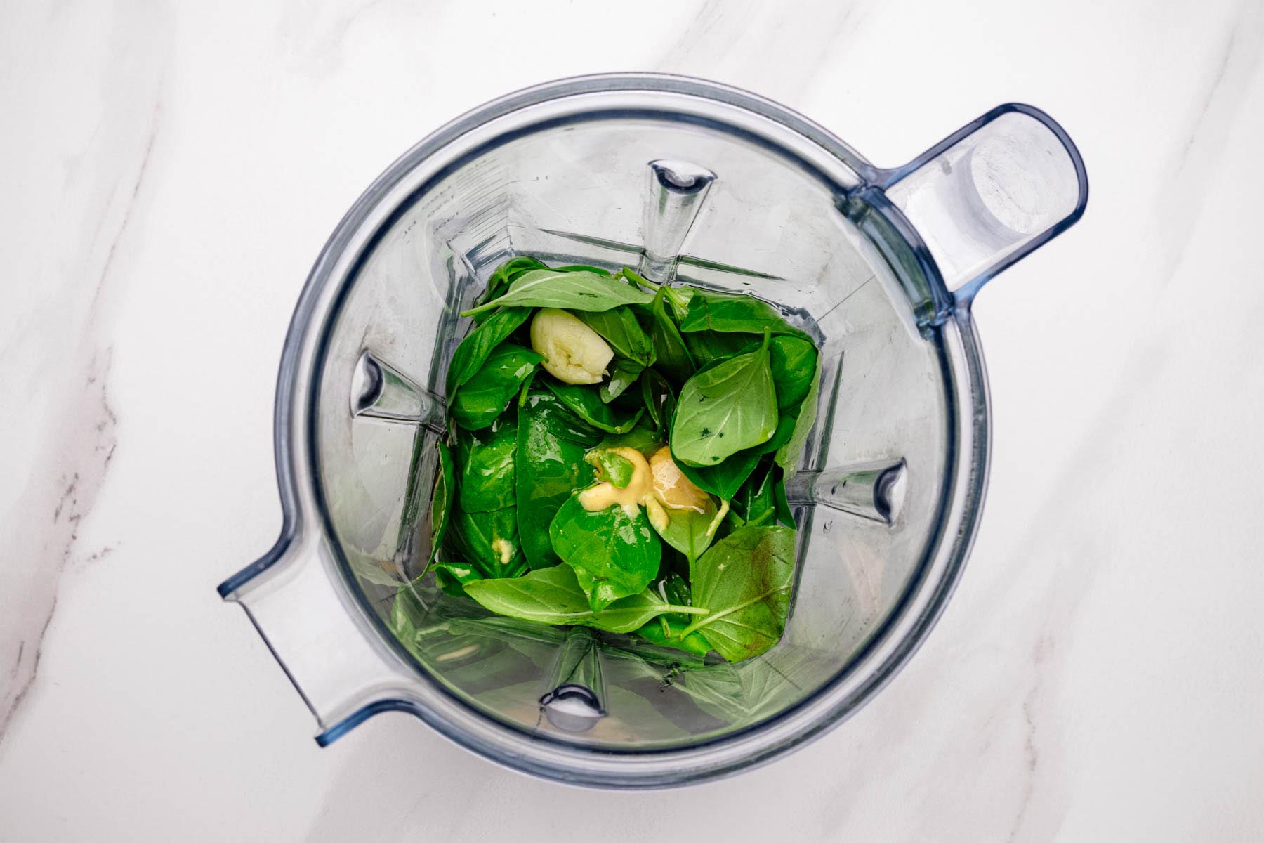 Fresh basil, garlic, and Dijon mustard in a blender, ready to be blended into basil vinaigrette.