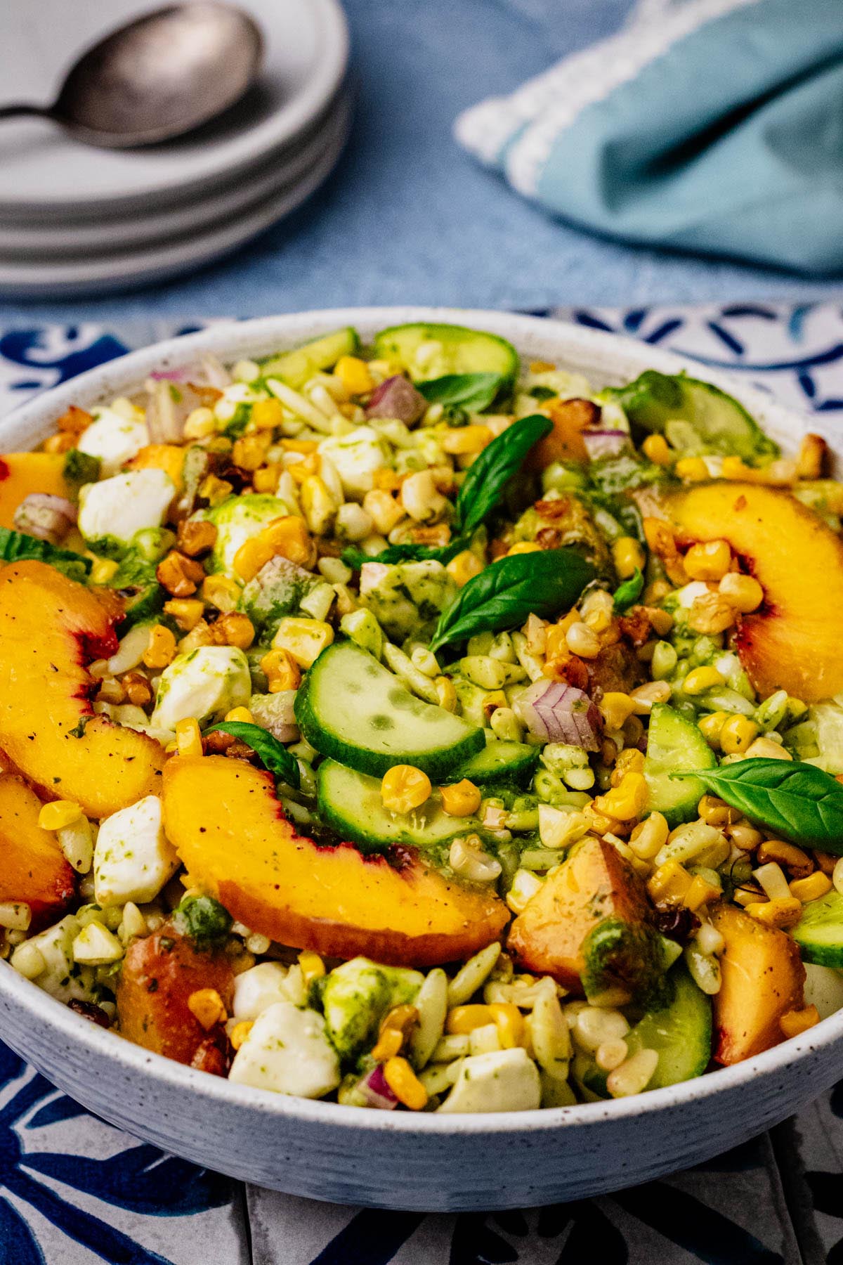 Summer orzo salad served in a bowl with grilled peaches, corn, cucumber, mozzarella, and basil vinaigrette, ready to serve.