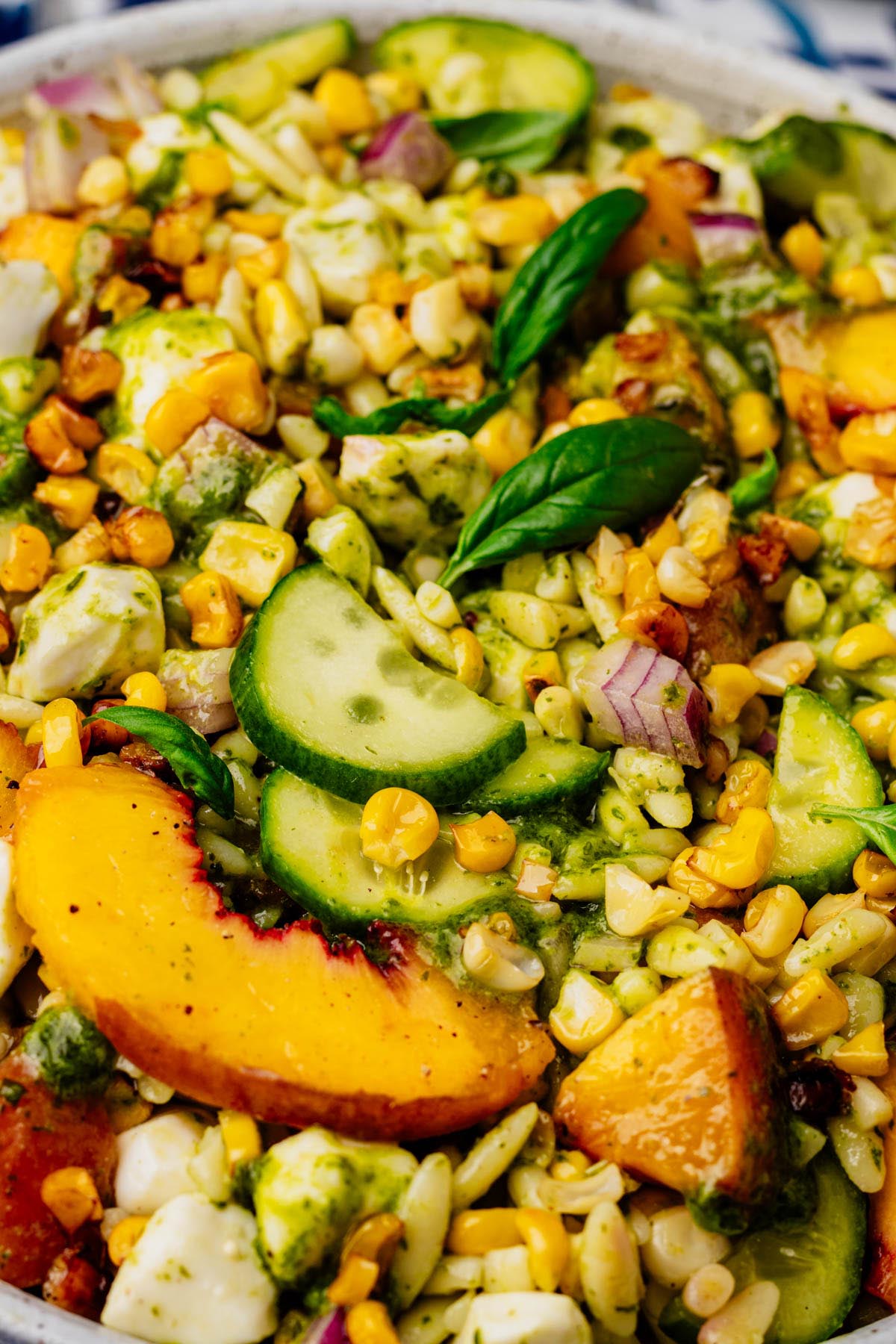 Close-up of summer orzo salad with grilled peaches, cucumber, corn, mozzarella, red onion, and basil vinaigrette.