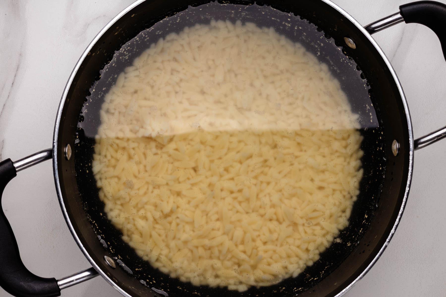 Orzo pasta boiling in a large pot of salted water on a white surface.