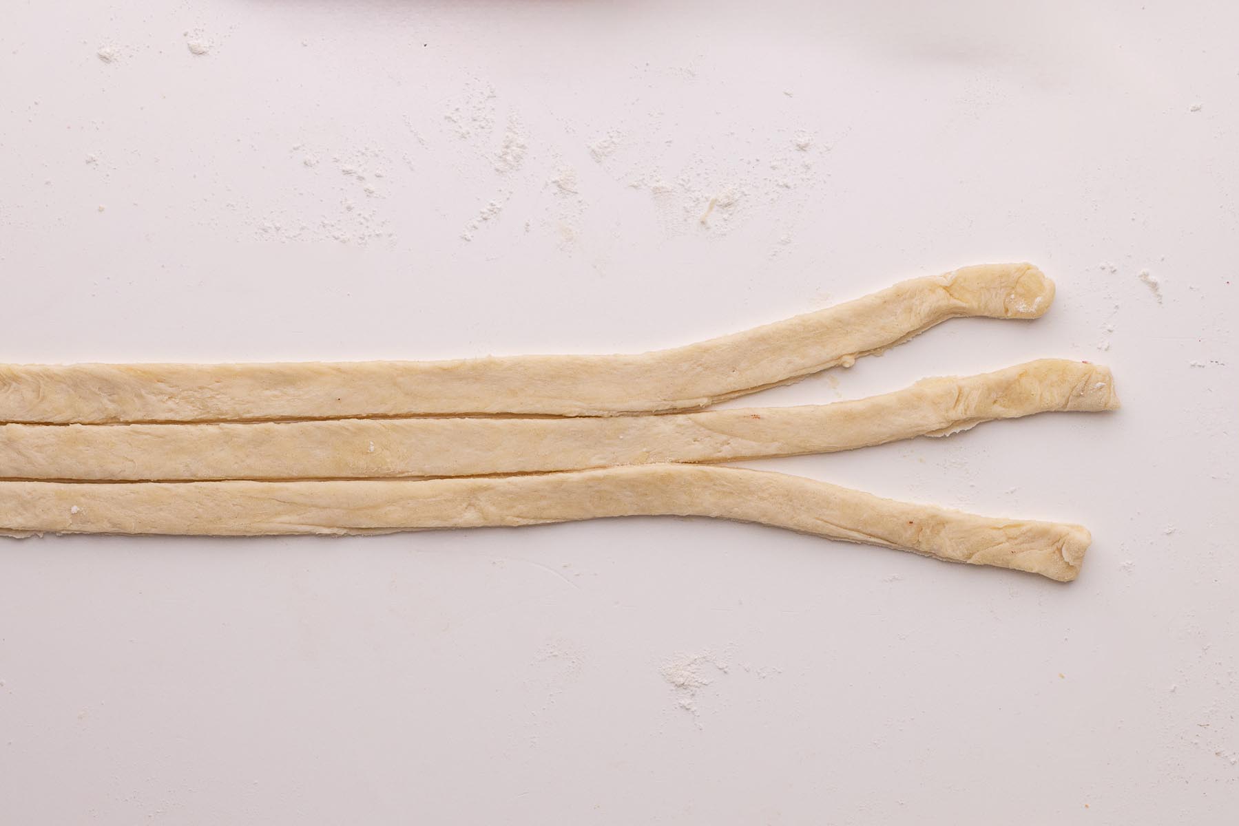 Three strips of pie dough positioned on a floured surface, ready to be braided for a decorative pie crust edge.
