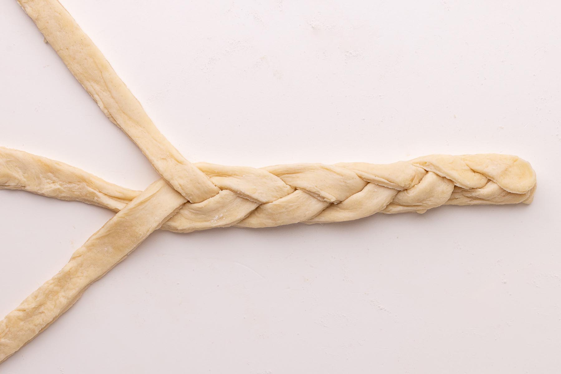 Three strips of pie dough braided together on a floured white surface to create a decorative crust edge.