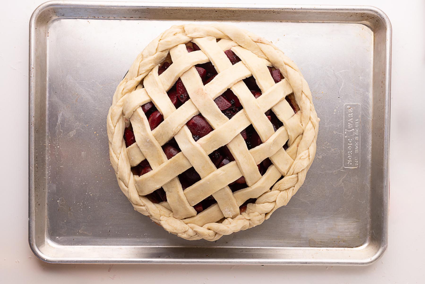 Unbaked pie with a woven lattice top and braided crust edge, placed on a metal baking sheet, ready to go into the oven.
