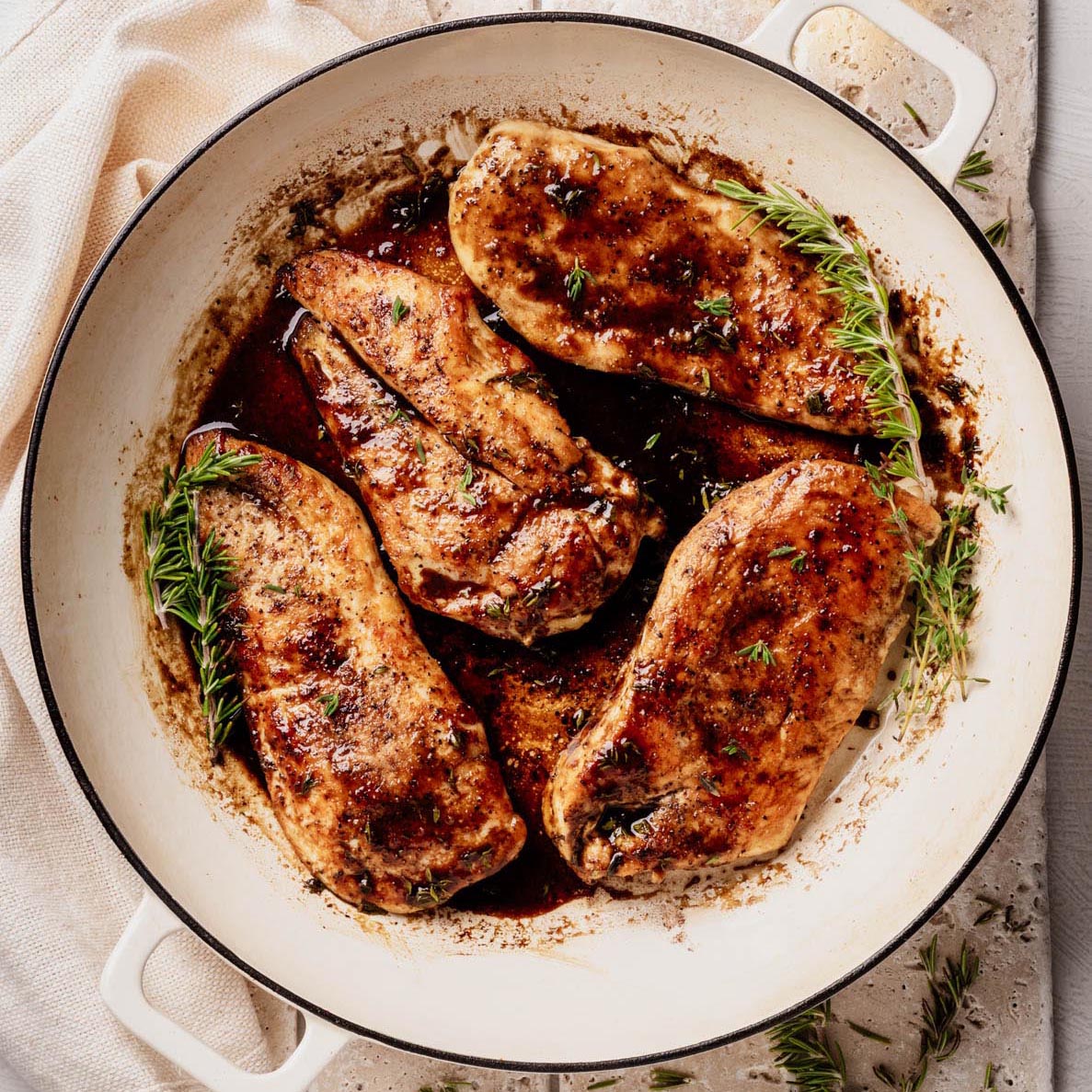 Golden-brown chicken cutlets in a glossy bourbon-maple glaze, garnished with fresh thyme and rosemary, in a white enameled skillet.