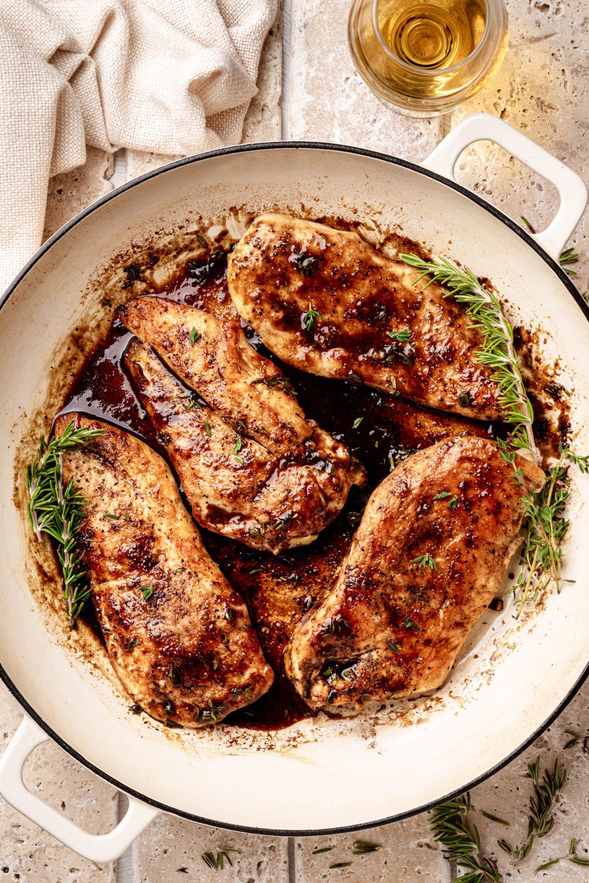 Golden-brown chicken cutlets in a glossy bourbon-maple glaze, garnished with fresh thyme and rosemary, in a white enameled skillet.