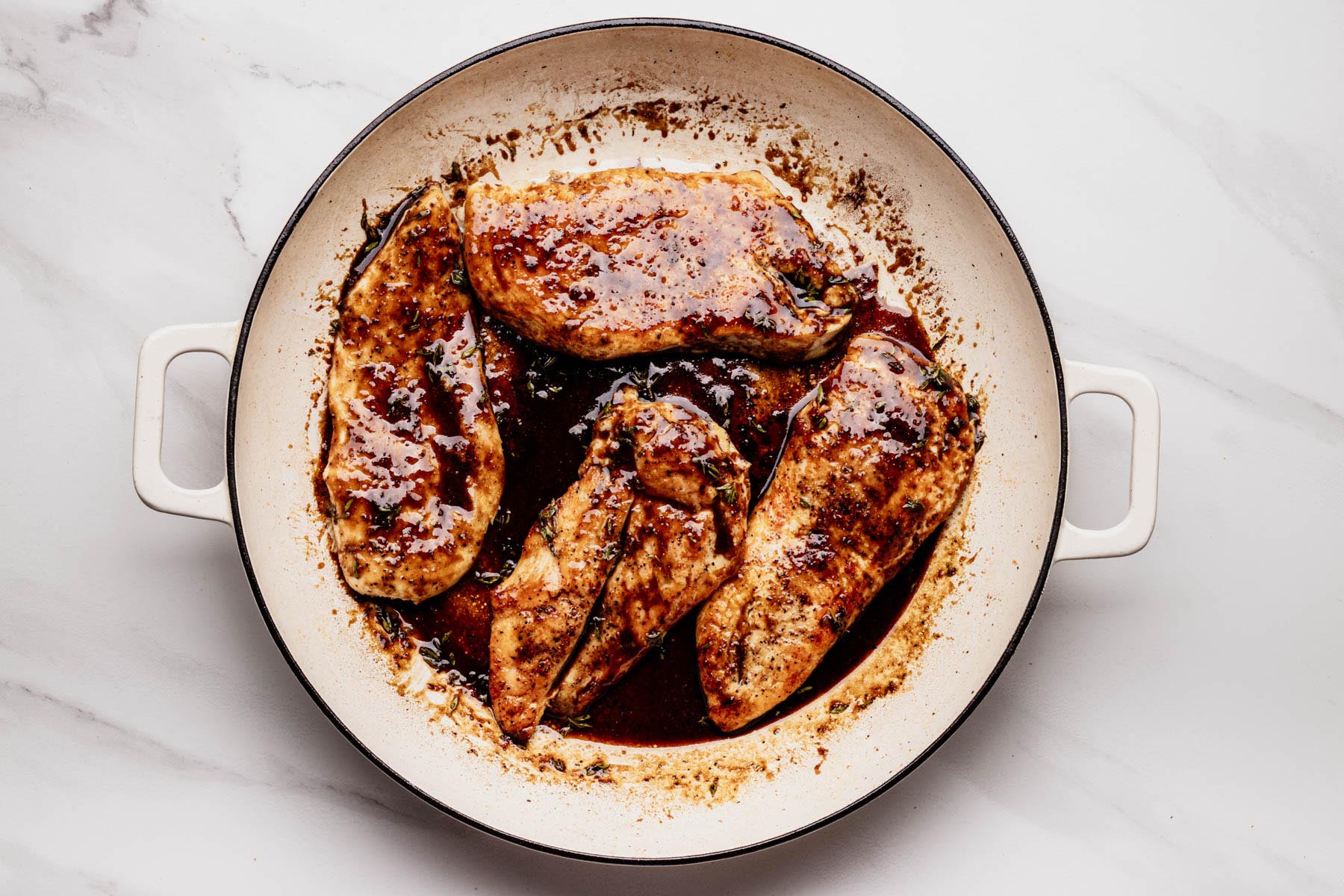 Chicken cutlets coated in glossy bourbon-maple glaze, simmering in a white enameled skillet with fresh thyme.