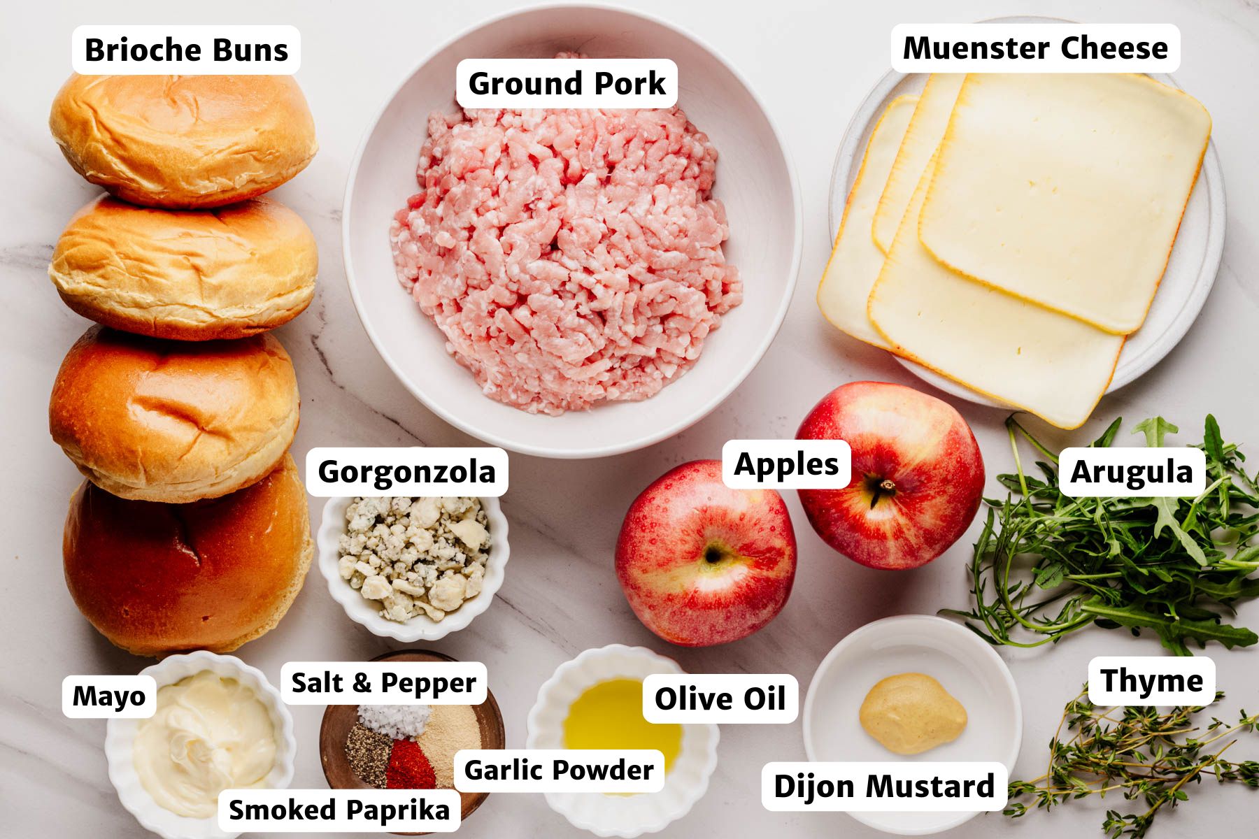 Labeled ingredients for ground pork burgers, including brioche buns, ground pork, Muenster cheese, arugula, apples, Gorgonzola, thyme, olive oil, Dijon mustard, mayo, smoked paprika, garlic powder, salt, and pepper.