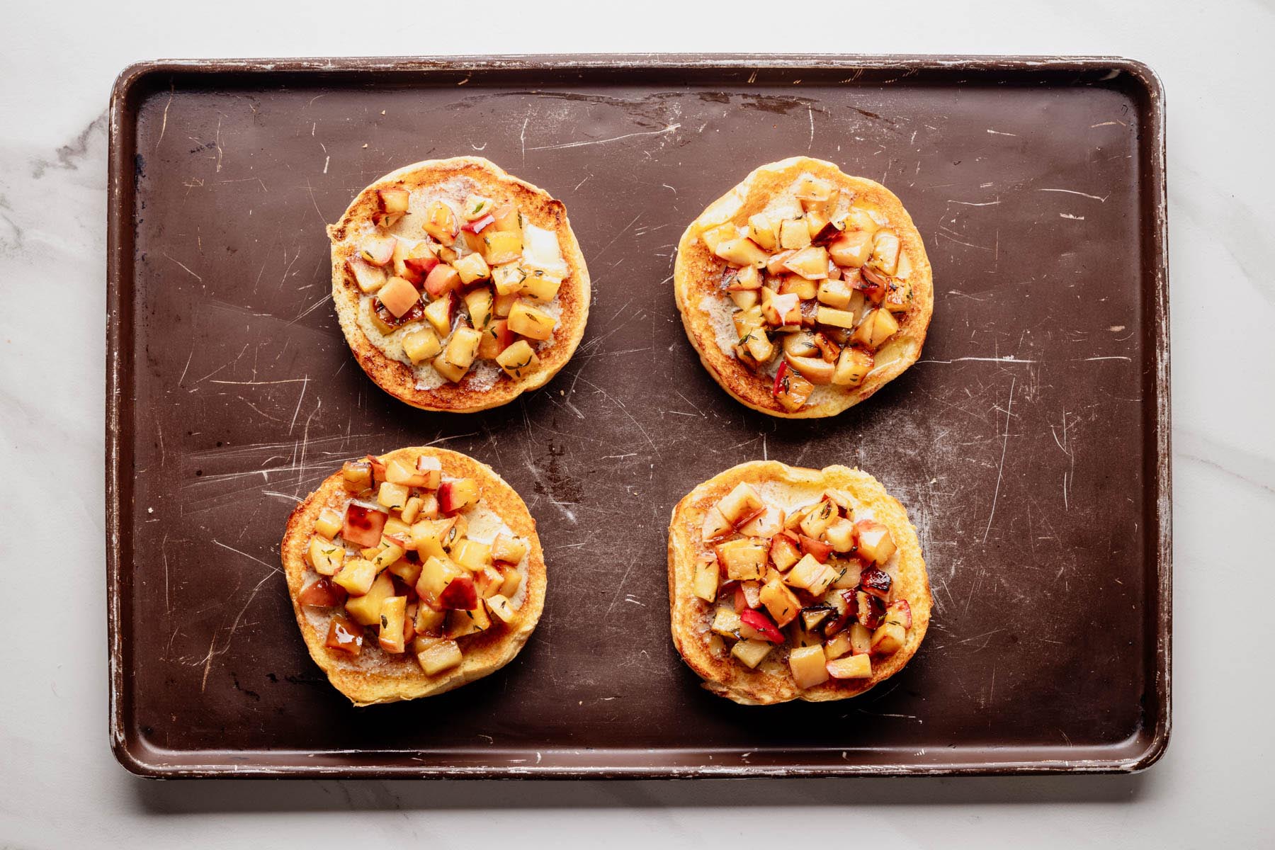 Toasted burger buns topped with saut&eacute;ed diced apples, arranged on a baking sheet.