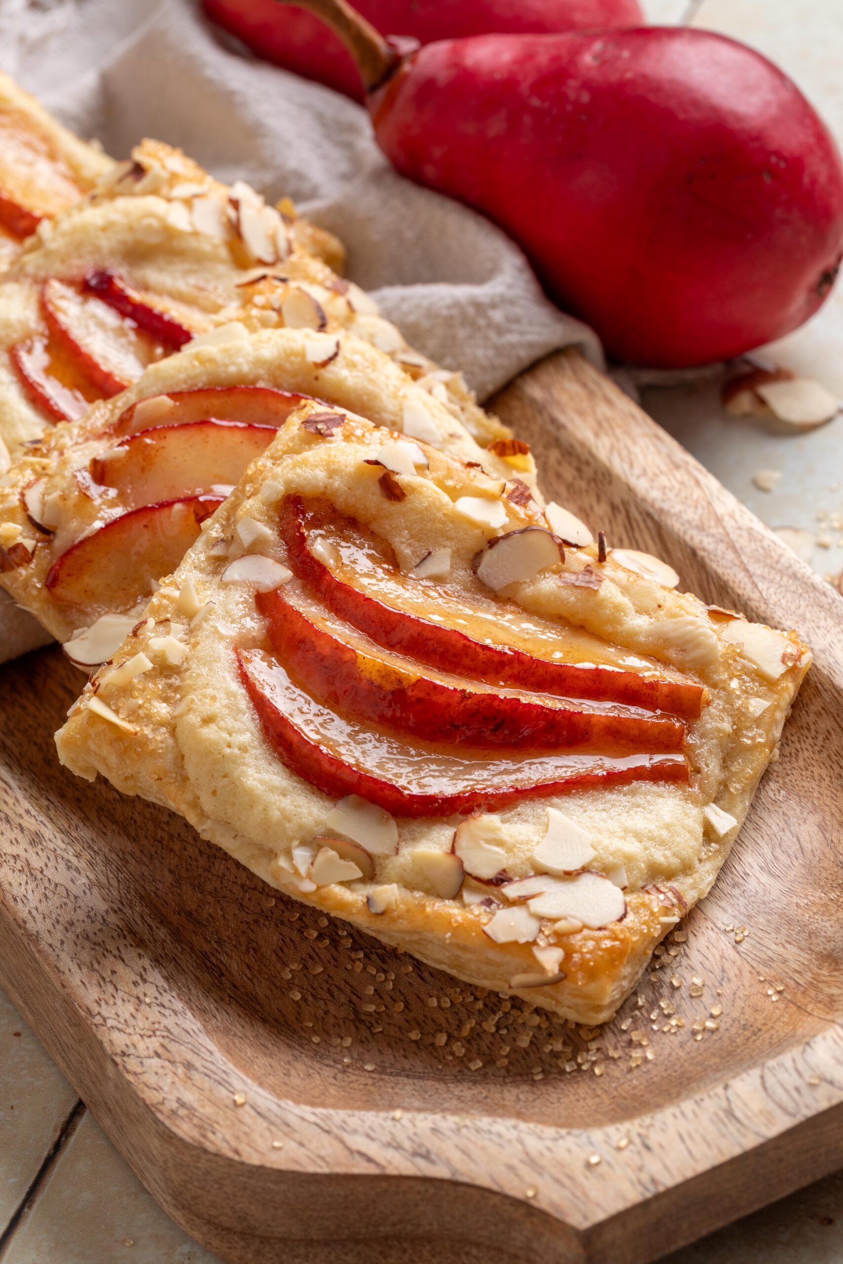 Close-up of pear puff pastry tart topped with red pear slices and slivered almonds on a wooden board.