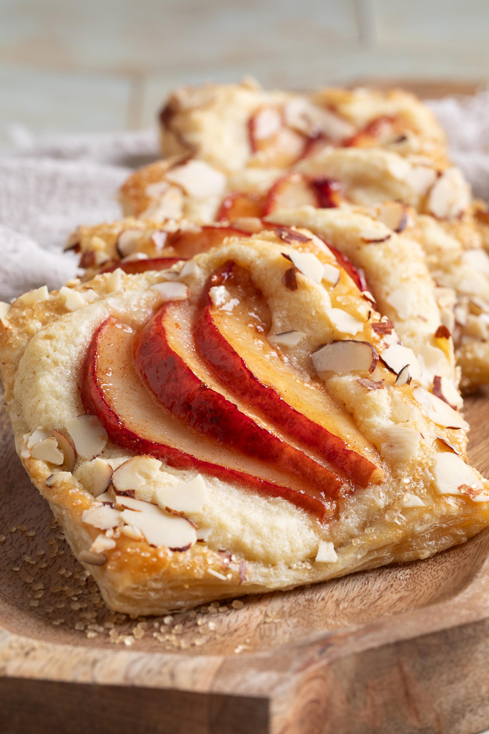 Close-up of a pear puff pastry tart topped with thin red pear slices and slivered almonds on a wooden board.