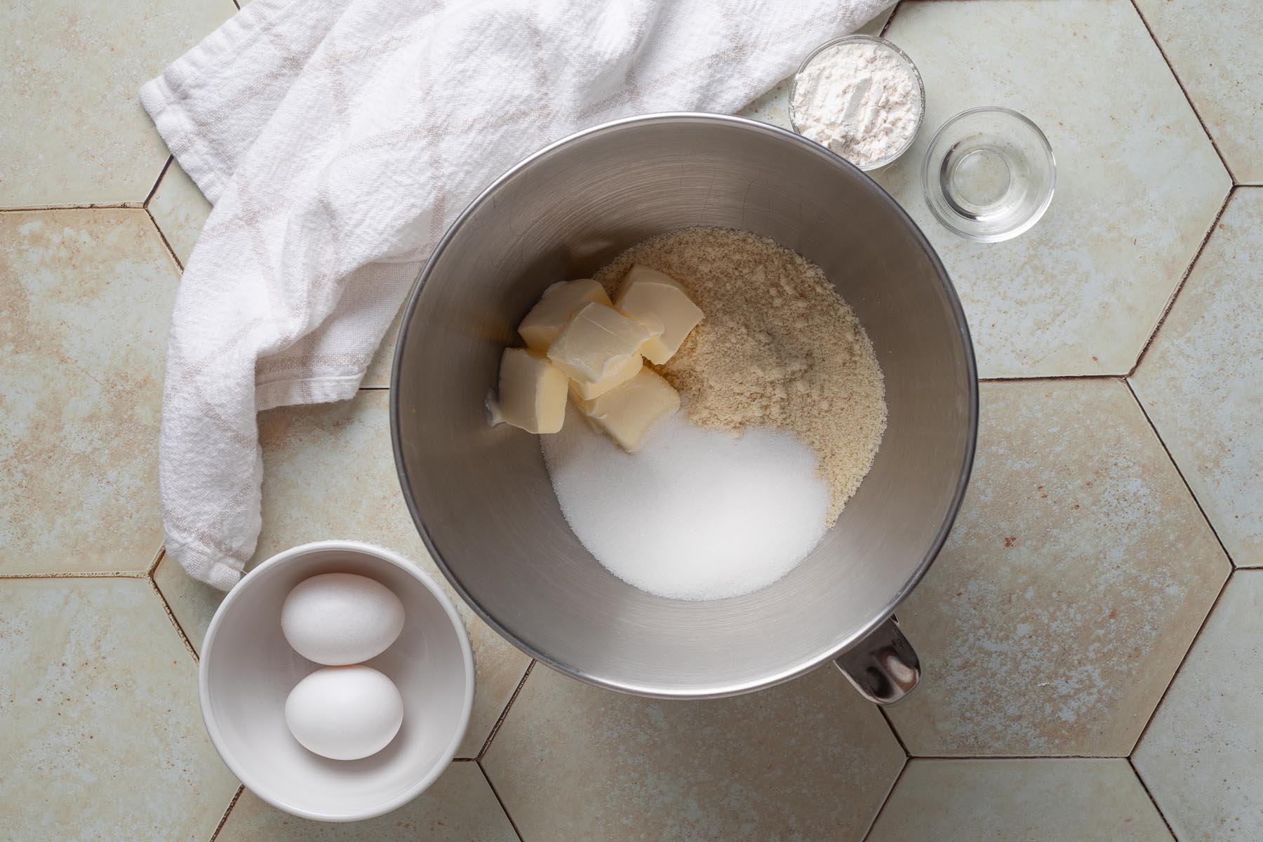 Butter, almond flour, and granulated sugar in a mixing bowl, ready to be creamed for the almond cream filling, with eggs, flour, and almond extract nearby on a tiled surface.