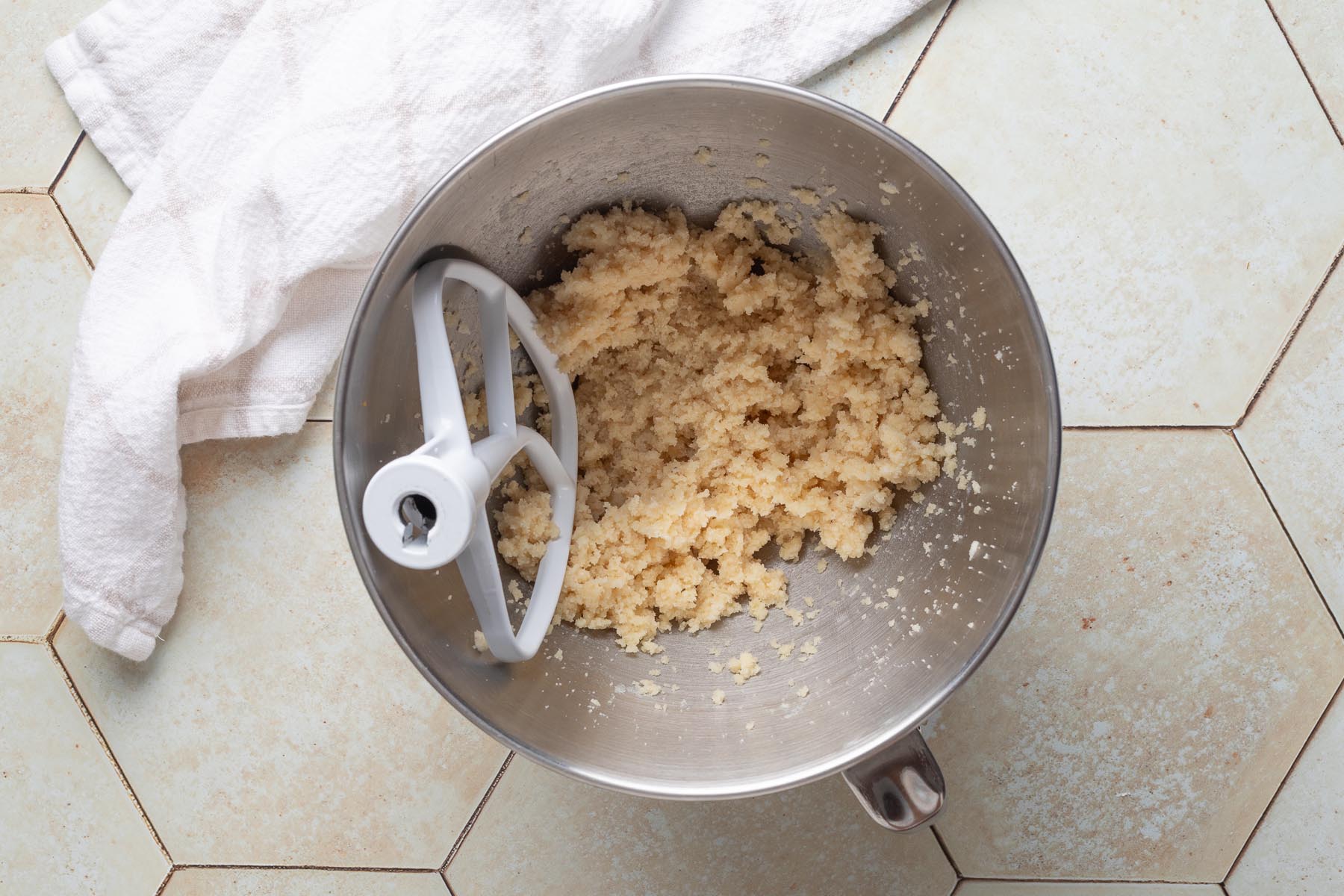 Creamed mixture of butter, almond flour, and sugar in a stand mixer bowl with a paddle attachment, showing the coarse and fluffy texture of the almond cream base.