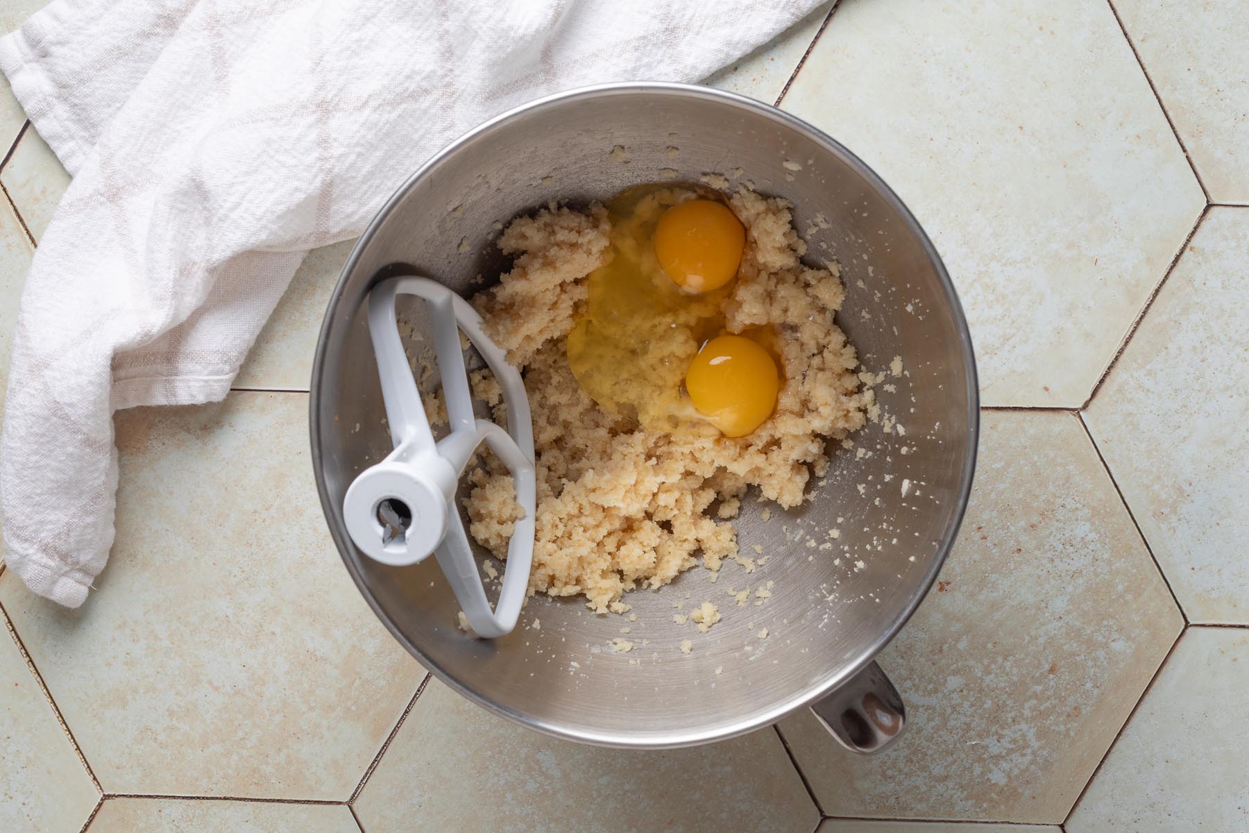 Two eggs added to the creamed almond flour, sugar, and butter mixture in a stand mixer bowl, ready to be mixed into the almond cream filling.