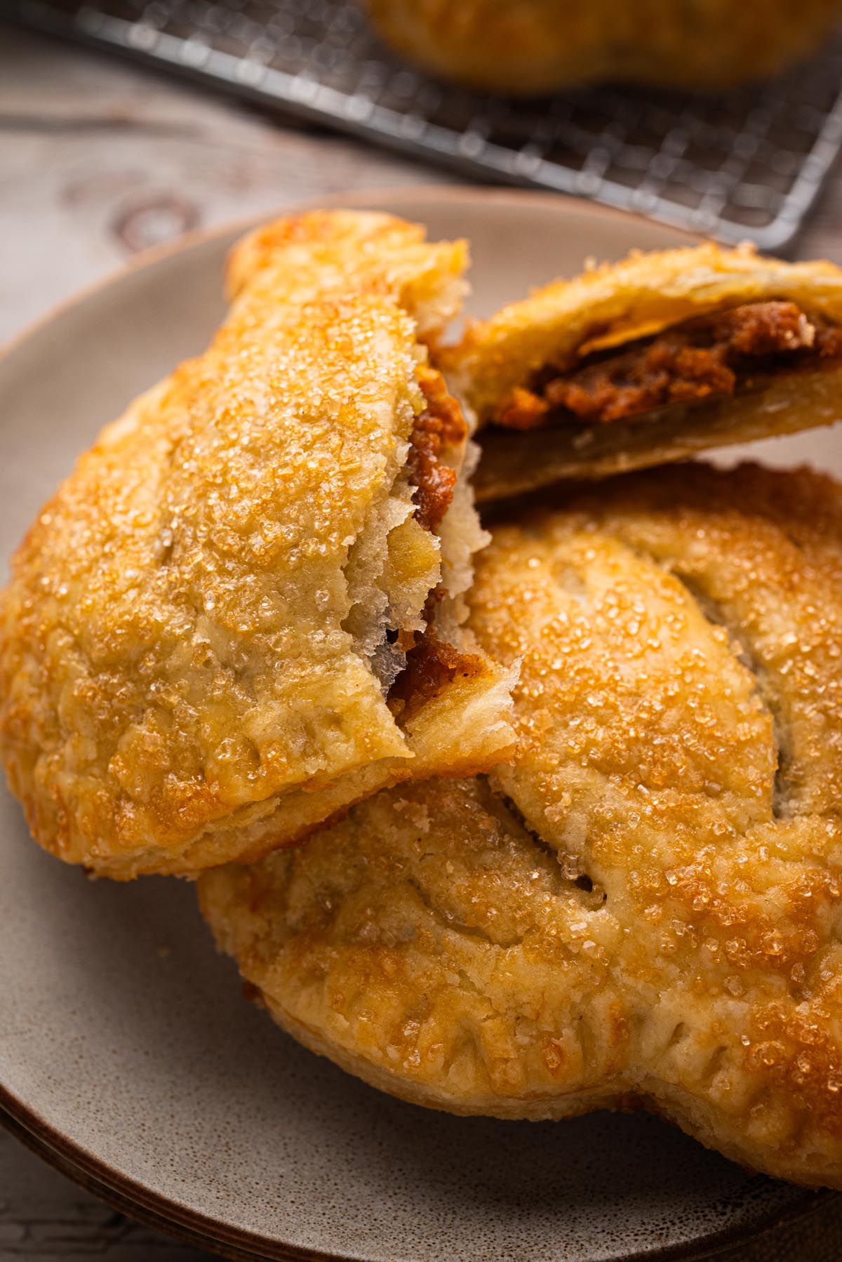 Pumpkin pie hand pie broken open on a plate, showing the spiced pumpkin filling inside a flaky golden crust with coarse sugar topping.