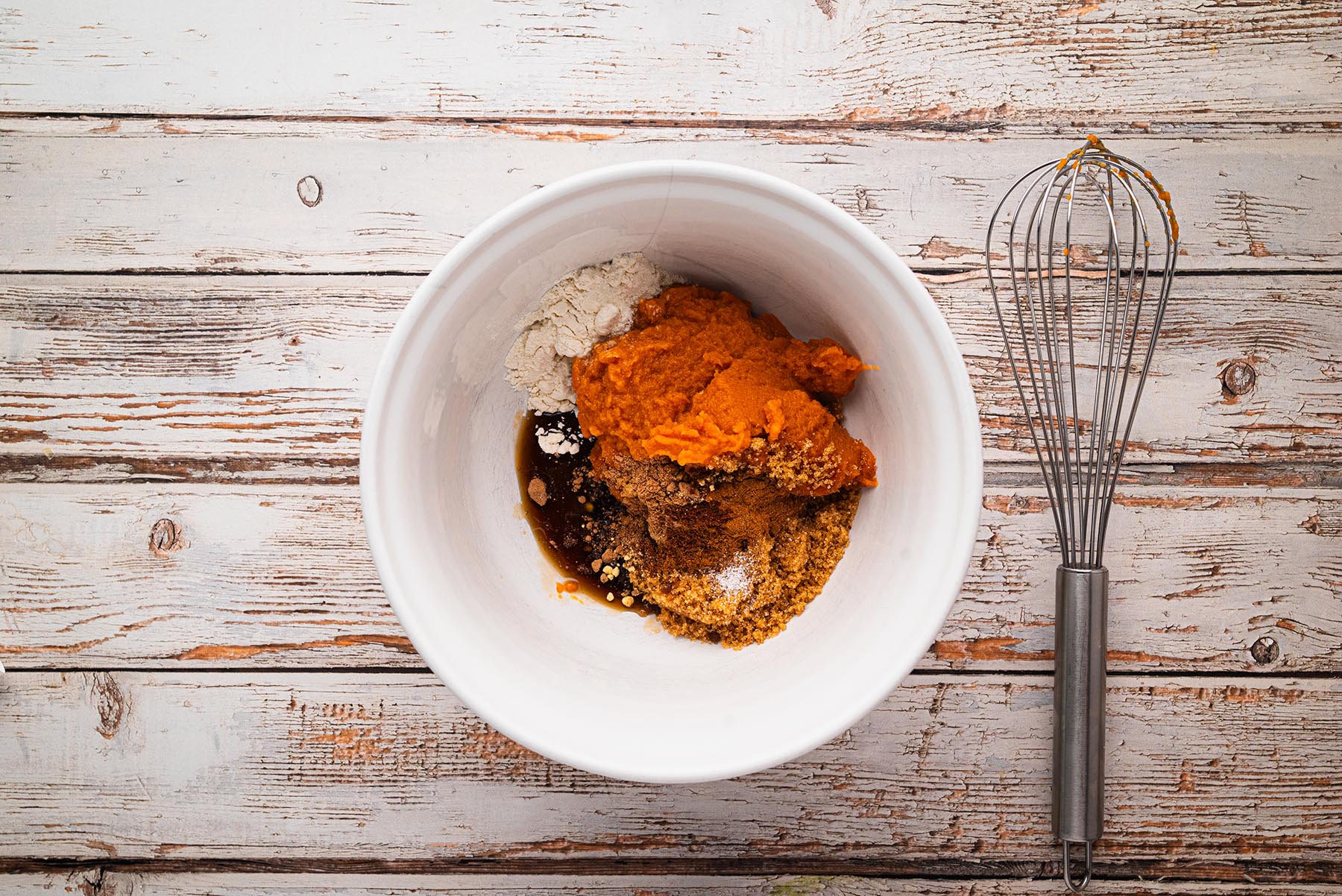 White mixing bowl with pumpkin purée, brown sugar, maple syrup, flour, and spices before being whisked together for pumpkin pie hand pie filling.