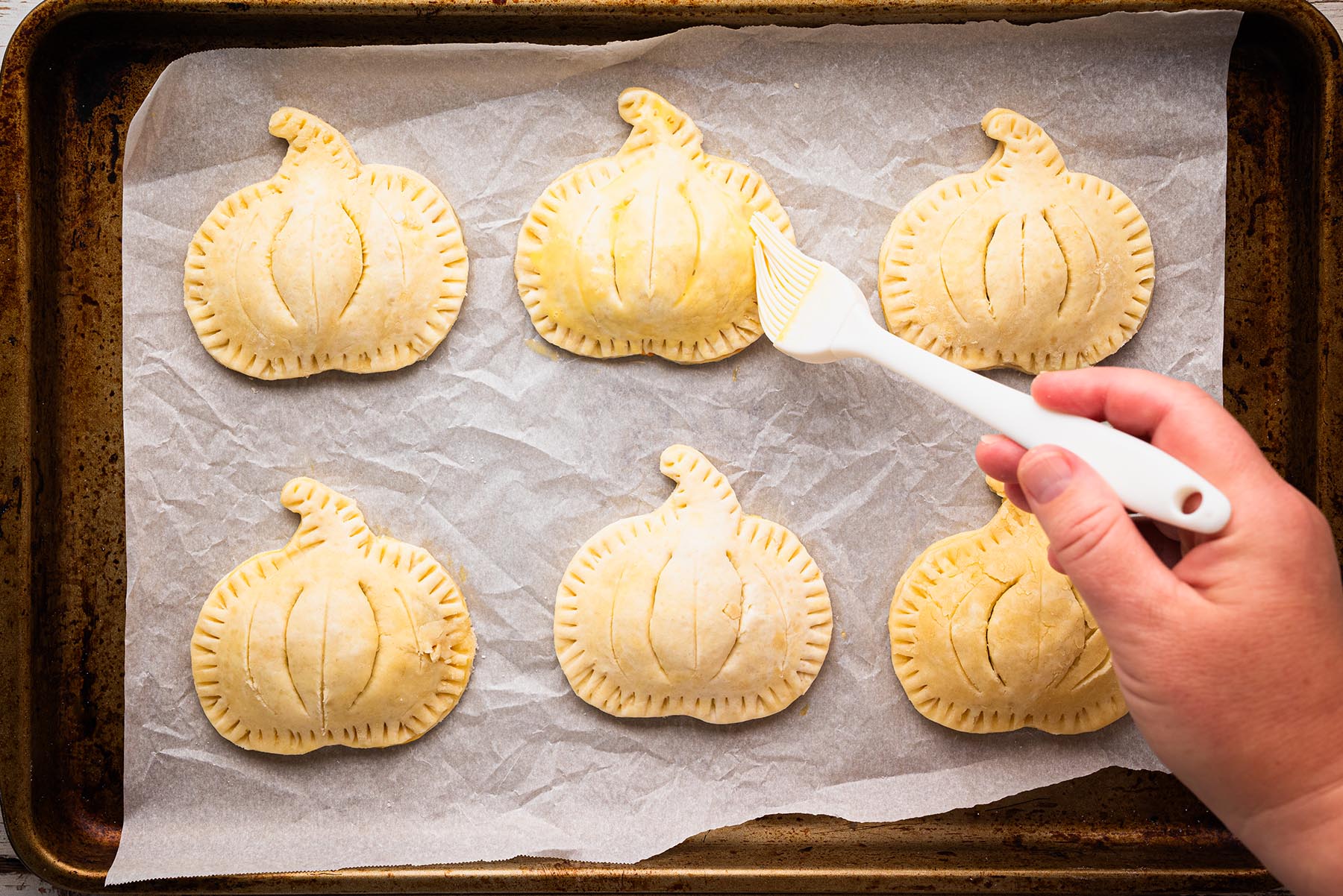 Pumpkin hand pies brushed with egg wash and sprinkled with coarse sugar before baking.