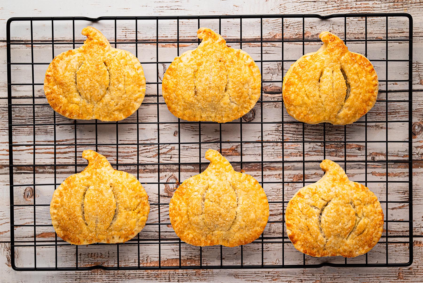 Golden brown pumpkin-shaped hand pies cooling on a black wire rack, sparkling with coarse sugar.