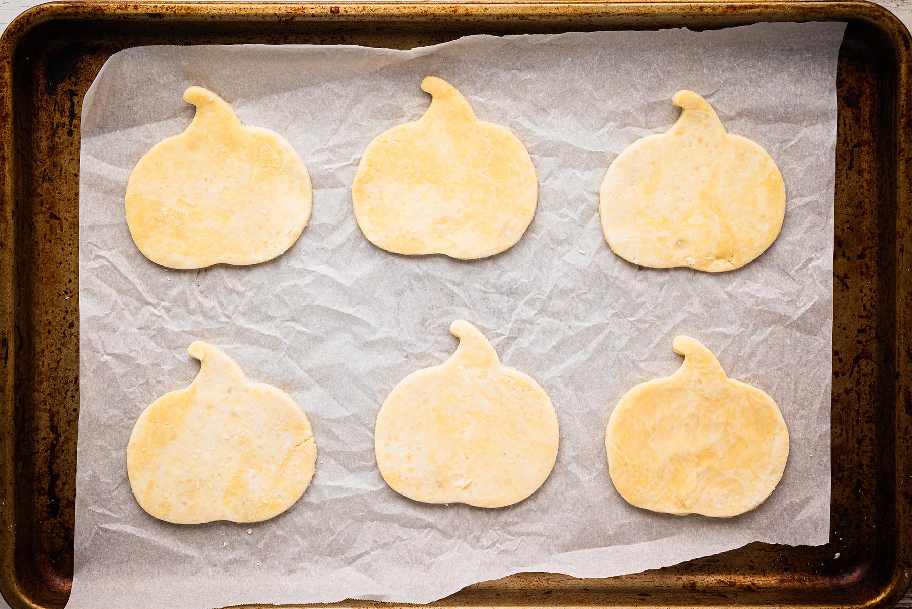 Pumpkin-shaped pie dough cutouts arranged on a parchment-lined baking sheet, ready to be filled for pumpkin pie hand pies.
