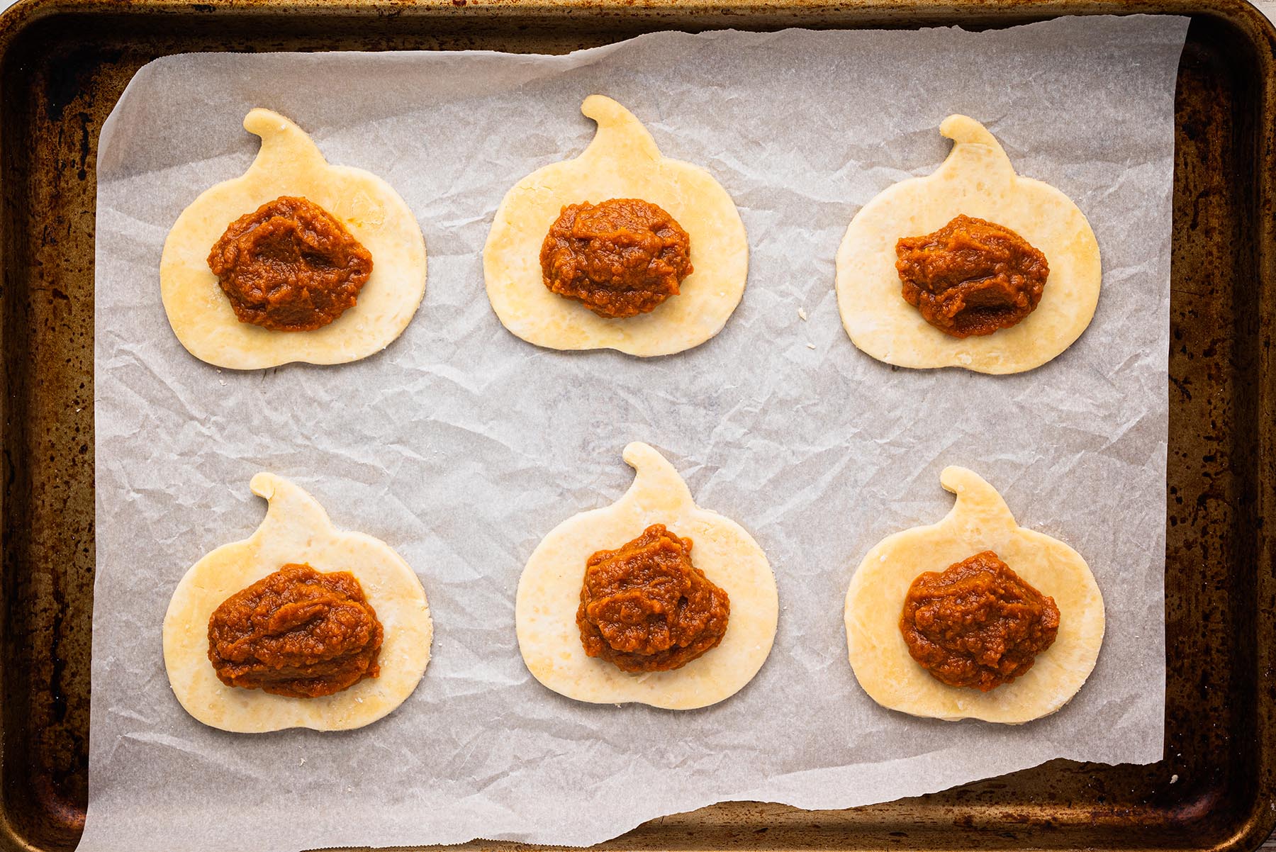 Dough rounds on a parchment-lined baking sheet with spoonfuls of pumpkin filling in the center.