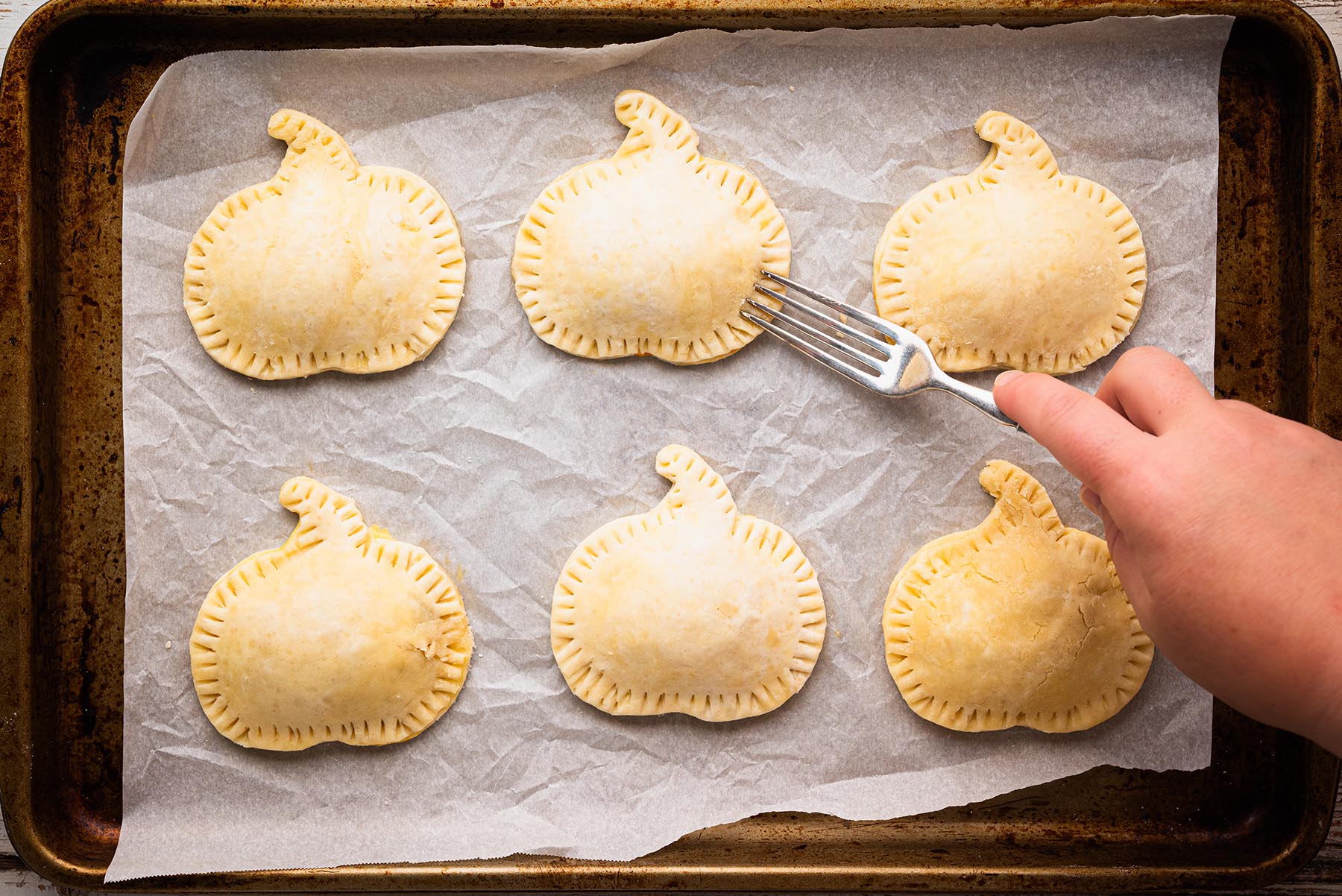 Fork crimping the edges of pumpkin hand pies to seal the filling inside.