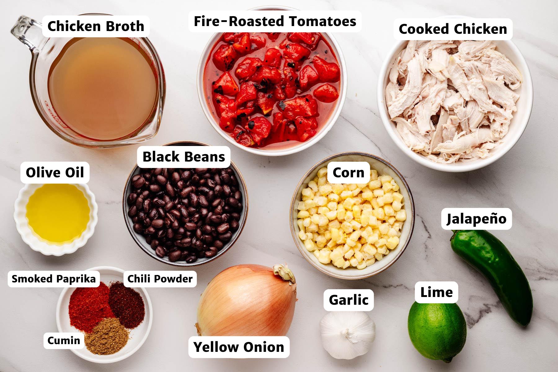 Labeled ingredients for Southwestern chicken soup including chicken broth, fire-roasted tomatoes, cooked chicken, olive oil, black beans, corn, jalapeño, garlic, yellow onion, lime, smoked paprika, cumin, and chili powder.