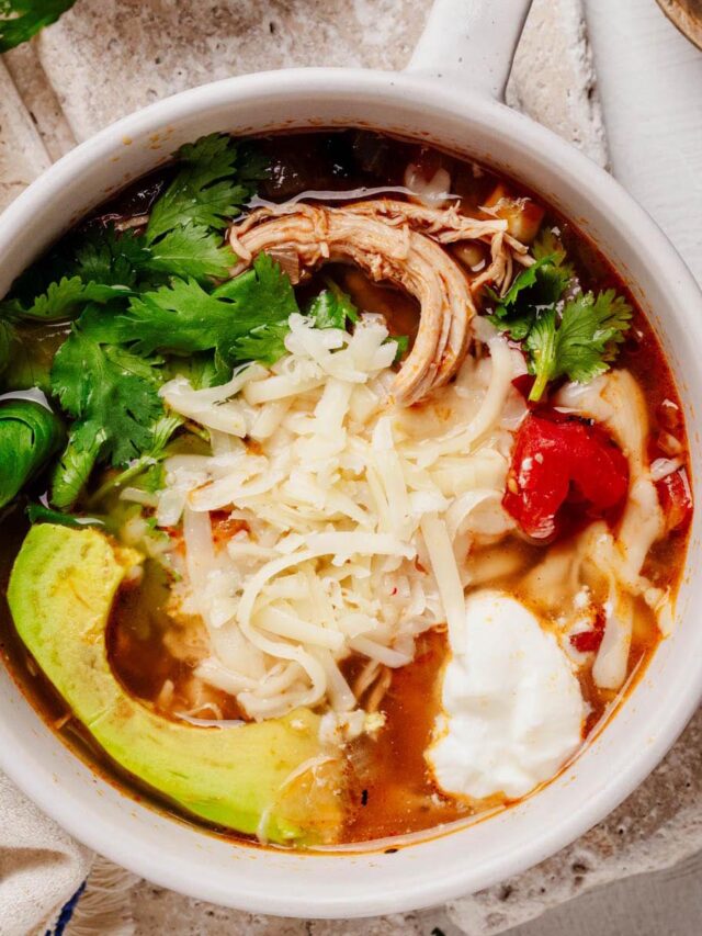 Bowl of Southwestern chicken soup topped with shredded cheese, avocado slices, cilantro, and sour cream.