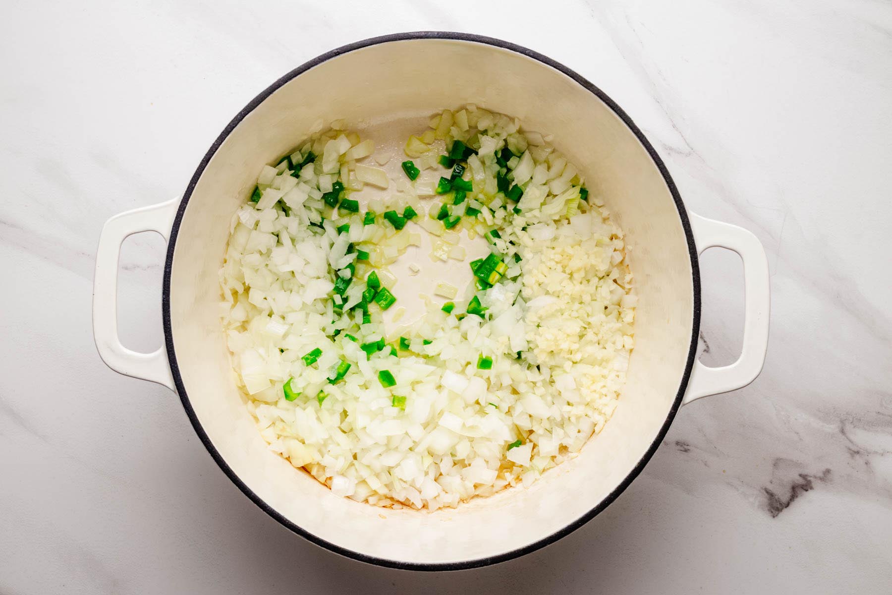 Diced onion, garlic, and jalapeño cooking in olive oil in a white Dutch oven.