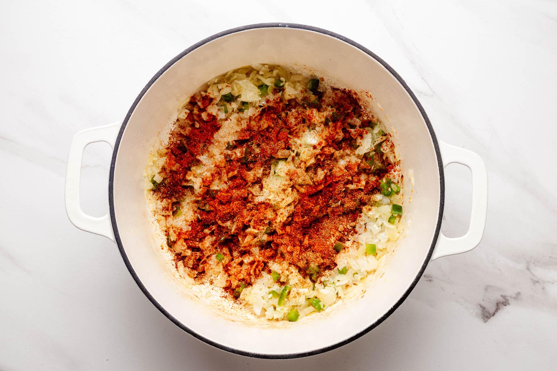Diced onion, garlic, and jalapeño in a Dutch oven with smoked paprika, cumin, and chili powder sprinkled on top.