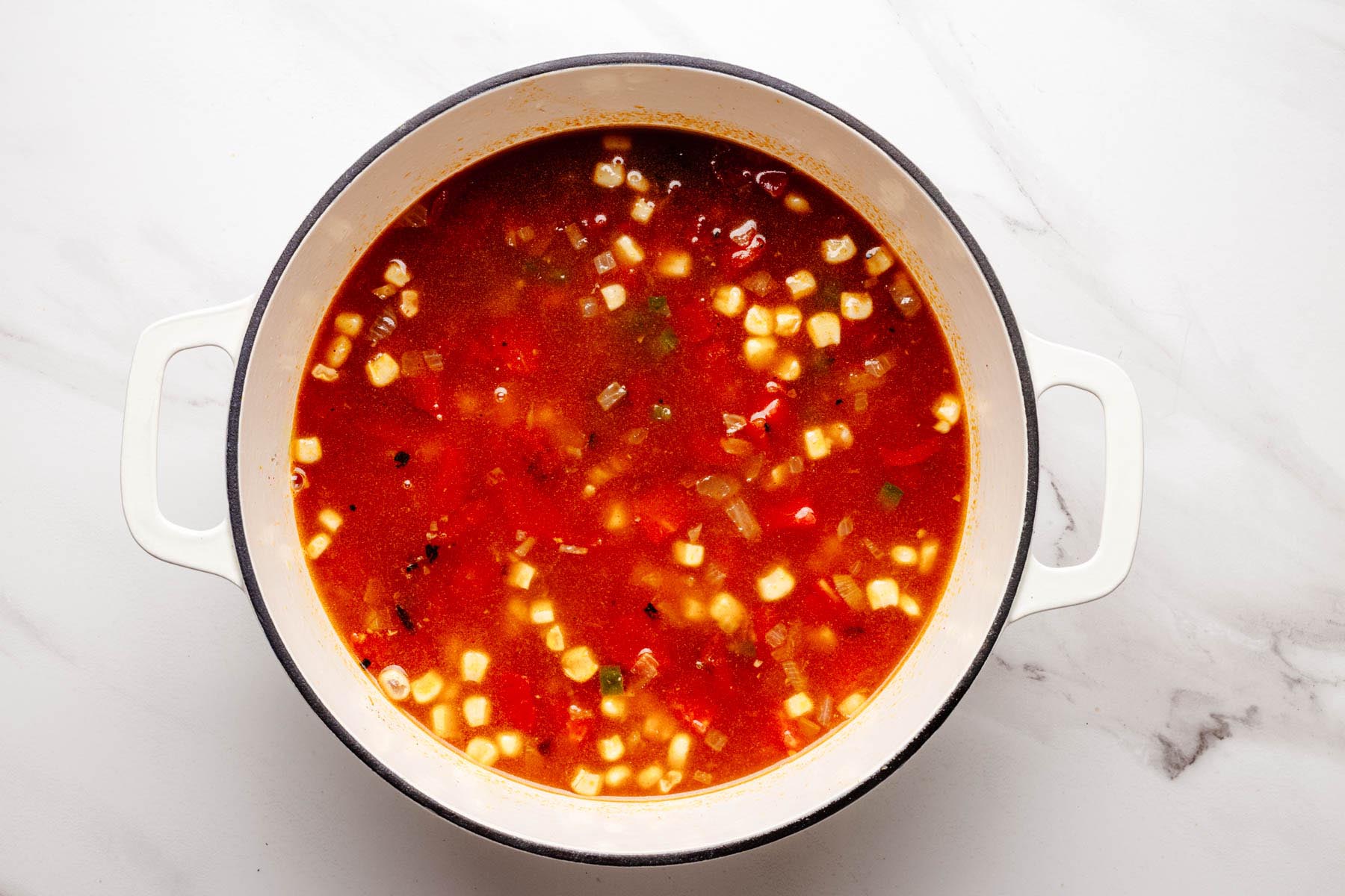 Dutch oven filled with chicken broth, fire-roasted tomatoes, corn, beans, and aromatics simmering together for Southwestern chicken soup.