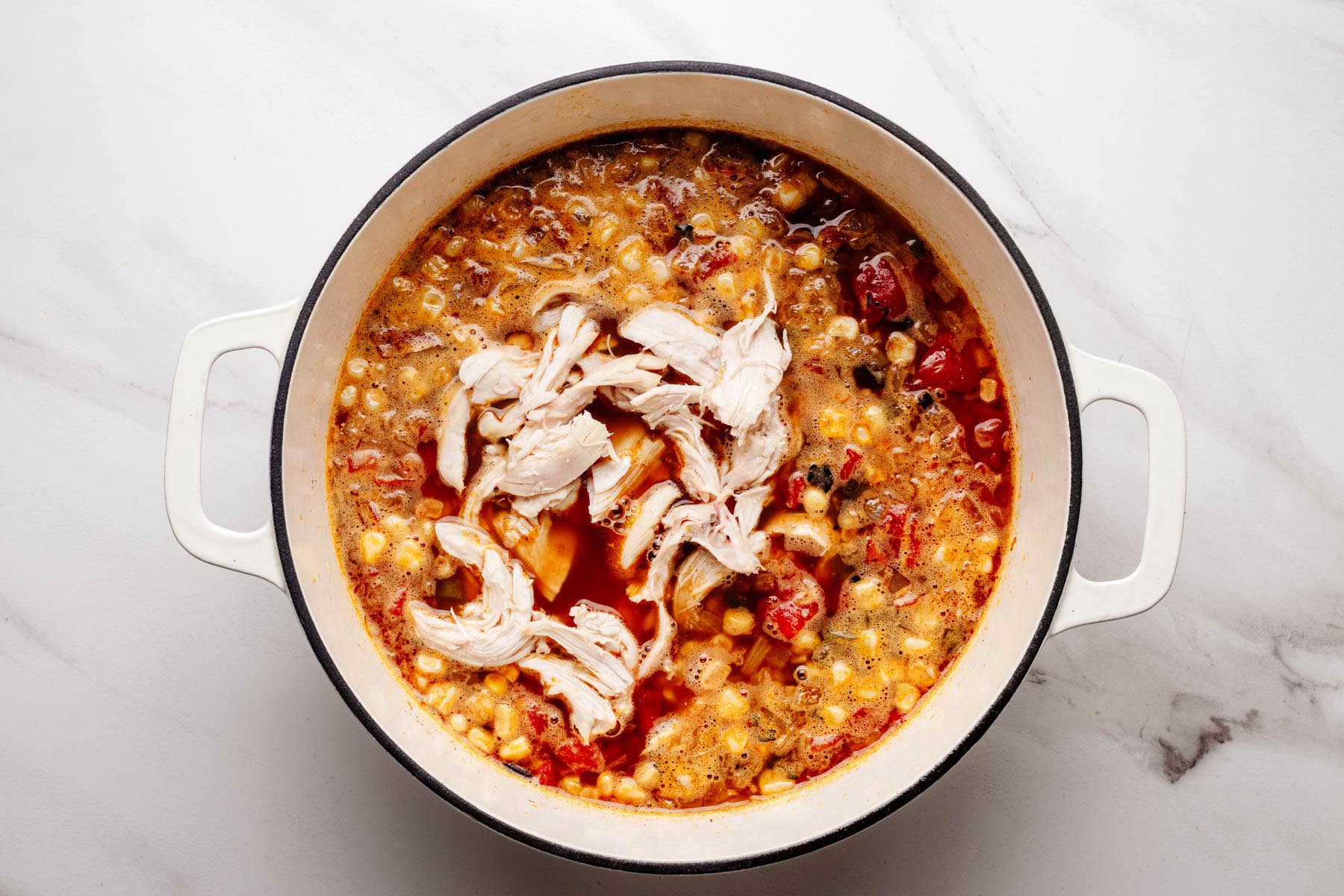 Shredded chicken added to a simmering pot of Southwestern chicken soup with corn and tomatoes.