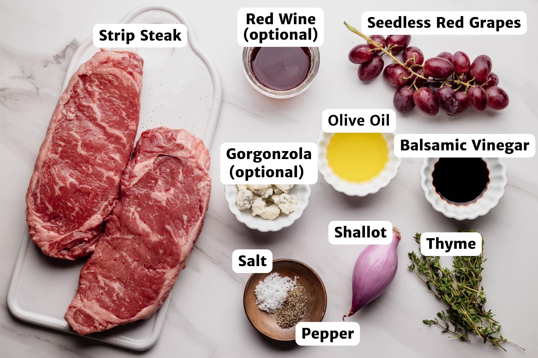 Labeled ingredients for cast iron strip steak with roasted grapes, including strip steak, seedless red grapes, shallot, thyme, balsamic vinegar, olive oil, salt, pepper, optional gorgonzola, and optional red wine.