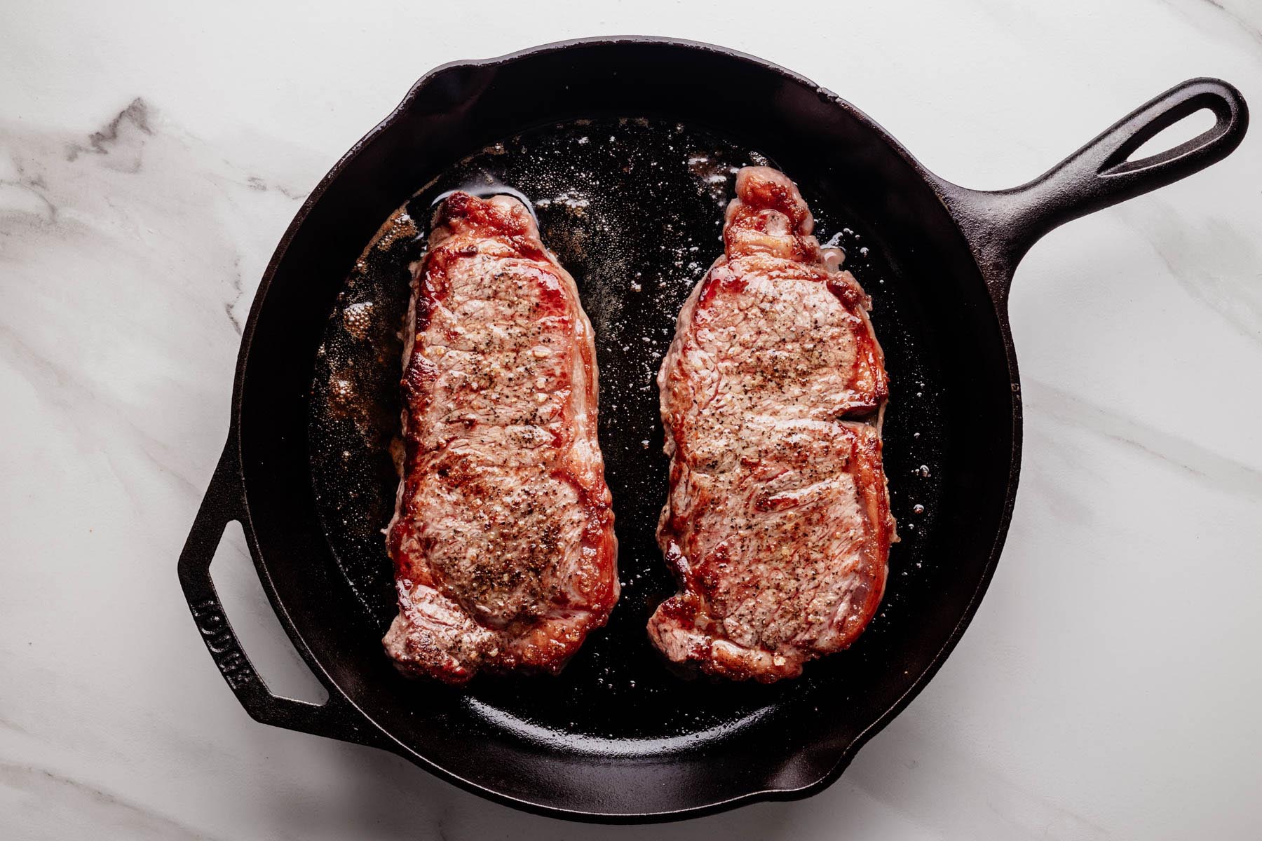 Two strip steaks searing in a cast iron skillet until browned and crusted.