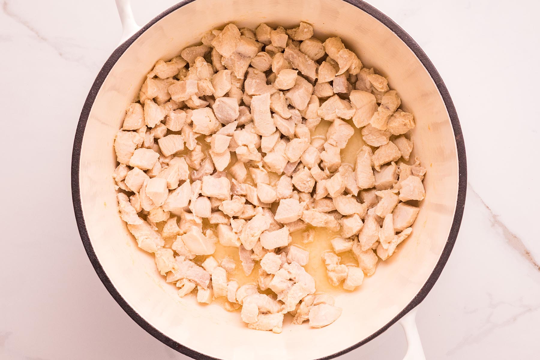 Cubed chicken cooking in a white Dutch oven, just turning opaque as it sears in olive oil.