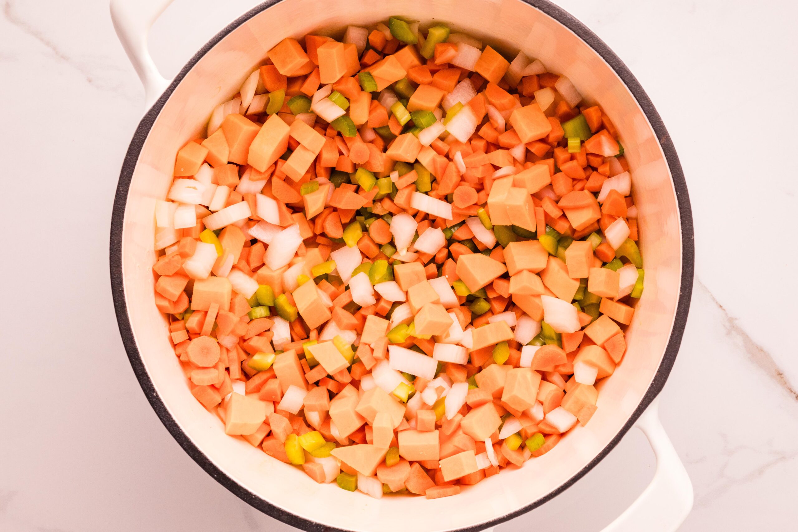 Diced carrots, celery, onion, and sweet potato saut&eacute;ing in a white Dutch oven after the chicken is removed.