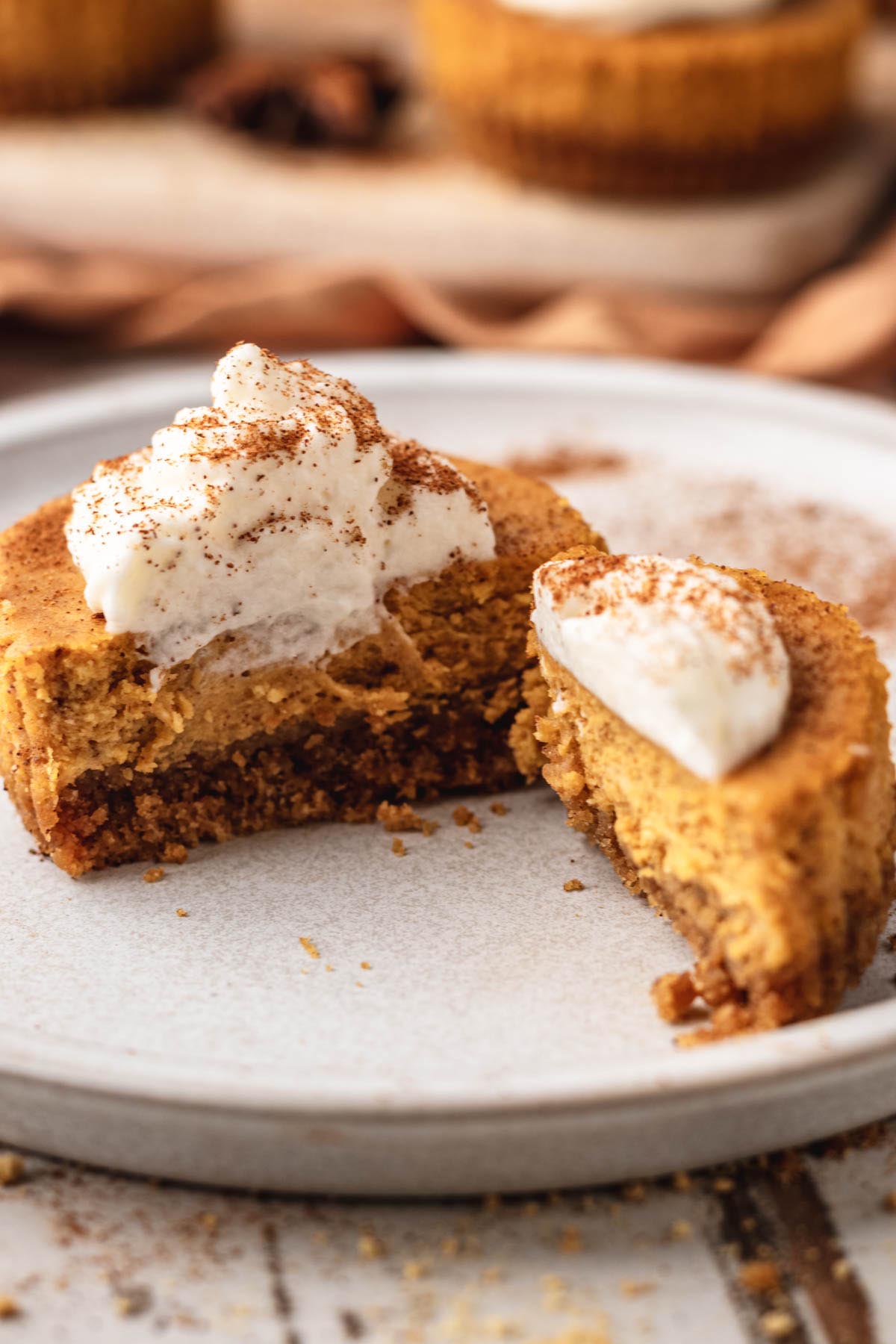 Mini pumpkin cheesecake cut in half on a white plate, showing graham cracker crust and creamy pumpkin filling, topped with whipped cream and dusted with cinnamon.