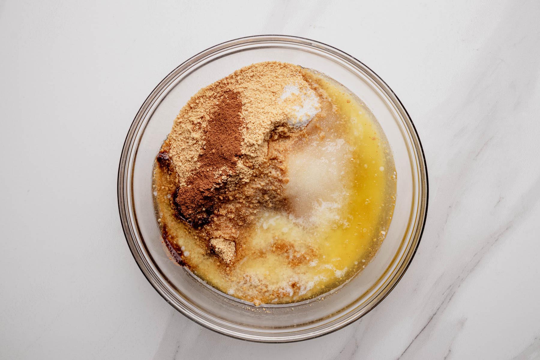 Glass bowl with graham cracker crumbs, sugar, cinnamon, and melted butter before mixing for cheesecake crust.