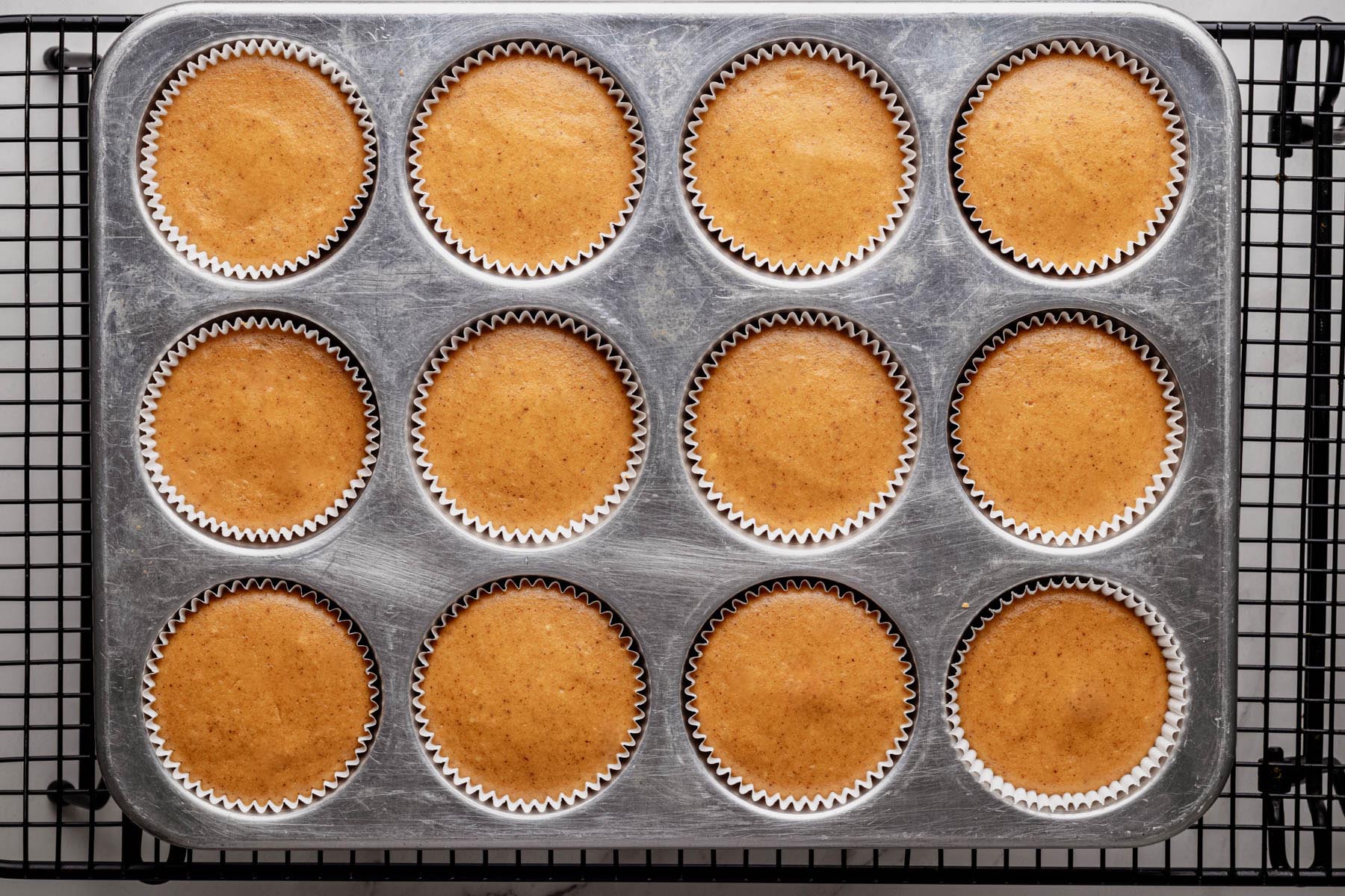 Muffin tin with baked mini pumpkin cheesecakes cooling on a wire rack.