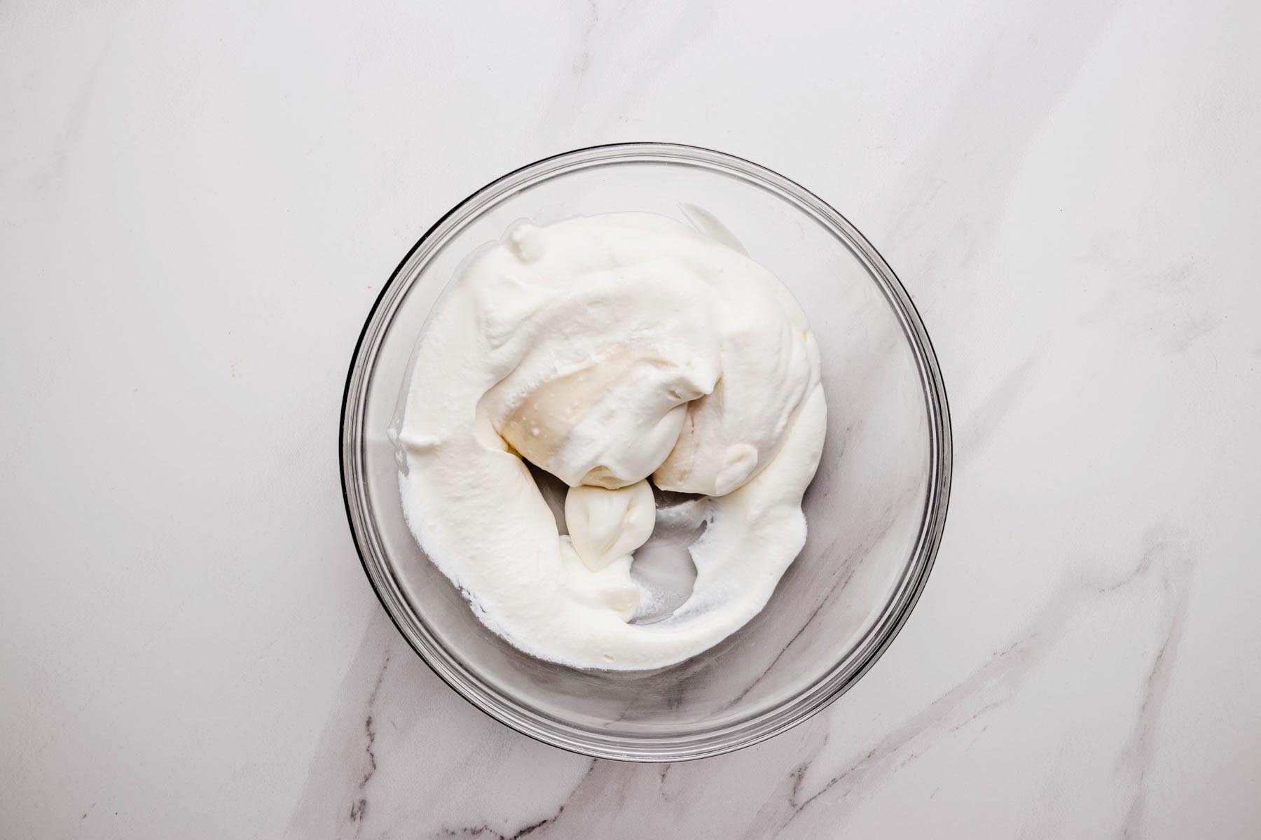 Whipped cream being folded into cream cheese mixture in a glass bowl.