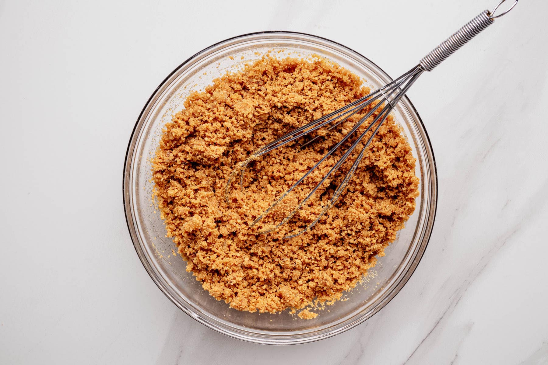 Glass bowl with graham cracker crust mixture stirred together with a whisk.