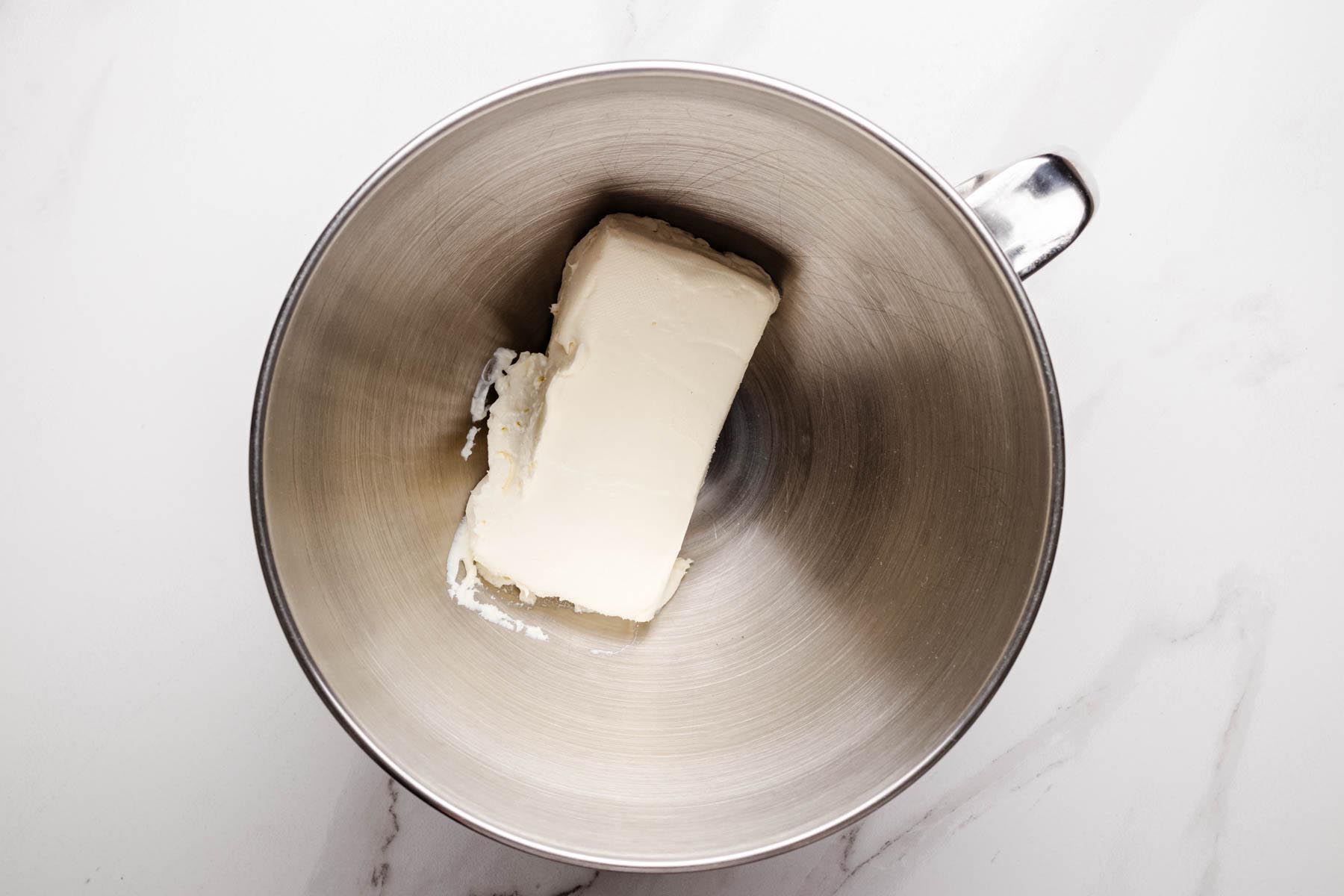 Block of cream cheese in a stainless steel mixing bowl.