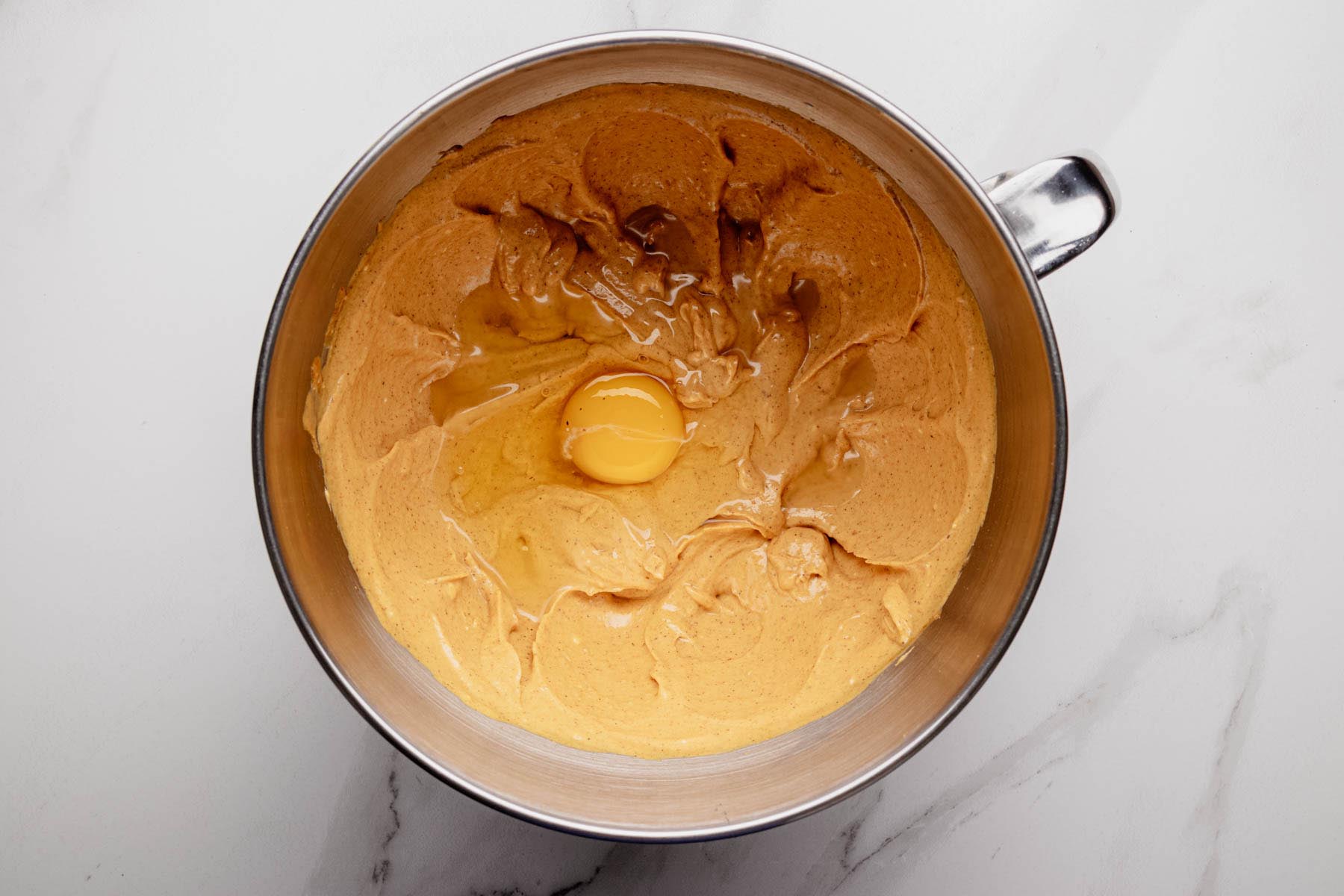 Pumpkin cheesecake batter in mixing bowl with an egg added on top before mixing.