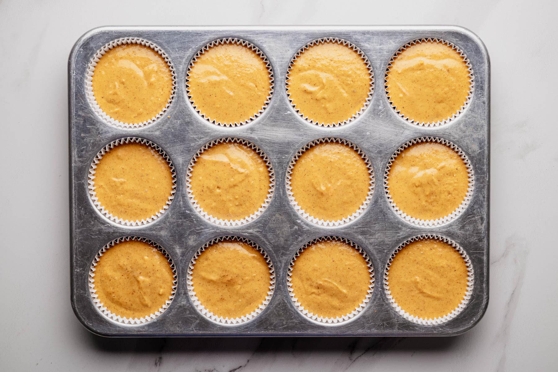 Muffin tin lined with paper cups filled with pumpkin cheesecake batter before baking.