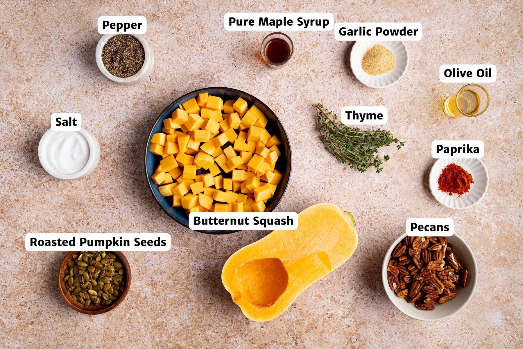 Labeled ingredients for maple roasted butternut squash including cubed squash, olive oil, maple syrup, thyme, pecans, pumpkin seeds, paprika, garlic powder, salt, and pepper.