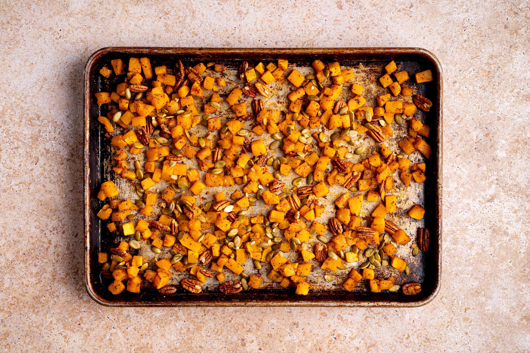 Sheet pan of roasted butternut squash cubes with pecans and pumpkin seeds after roasting.