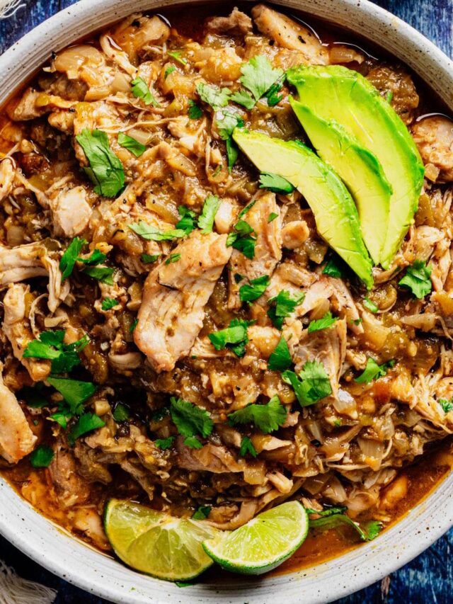 Bowl of shredded green chili chicken topped with avocado slices, fresh cilantro, and lime wedges.
